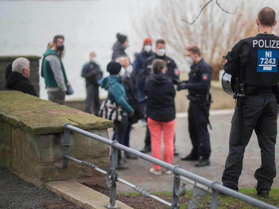 Polizisten stehen vor einer Menschengruppe an der Löwenbastion am Maschsee. Die Polizei Hannover hat einen sogenannten „Corona-Spaziergang“ - eine unangemeldete Veranstaltung mit mehreren Personen als Protest gegen die staatlichen Corona-Maßnahmen - kurzerhand als unangemeldete Demonstration bewertet. Das Symbolbild wurde am zweiten Januar 2022 aufgenommen.