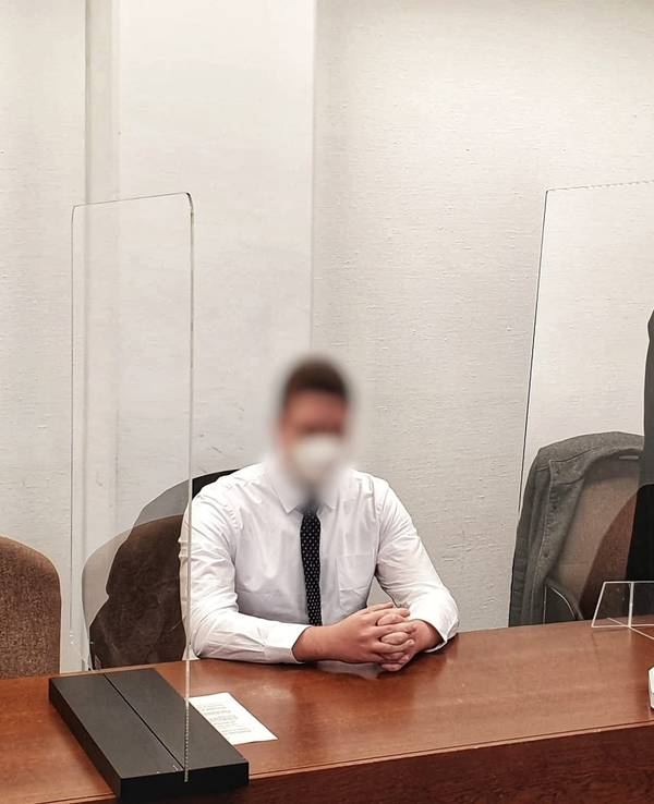 Ein junger Mann sitzt mit gefalteten Händen auf der Anklagebank, neben ihm steht sein Verteidiger.