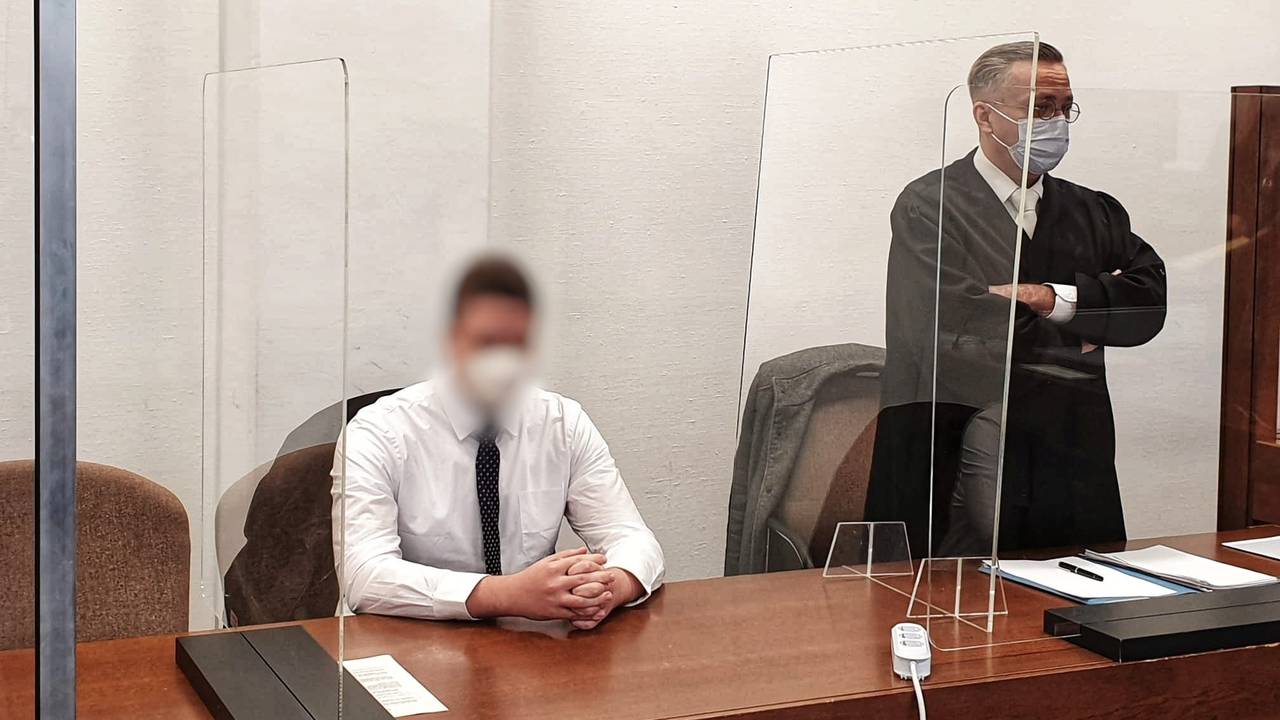 Ein junger Mann sitzt mit gefalteten Händen auf der Anklagebank, neben ihm steht sein Verteidiger.