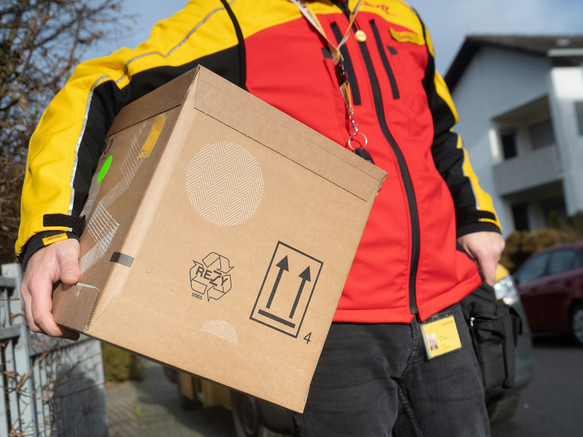Ein DHL-Mitarbeiter trägt ein Paket unter seinem Arm. Das Symbolbild wurde am 15. Dezember 2021 aufgenommen.