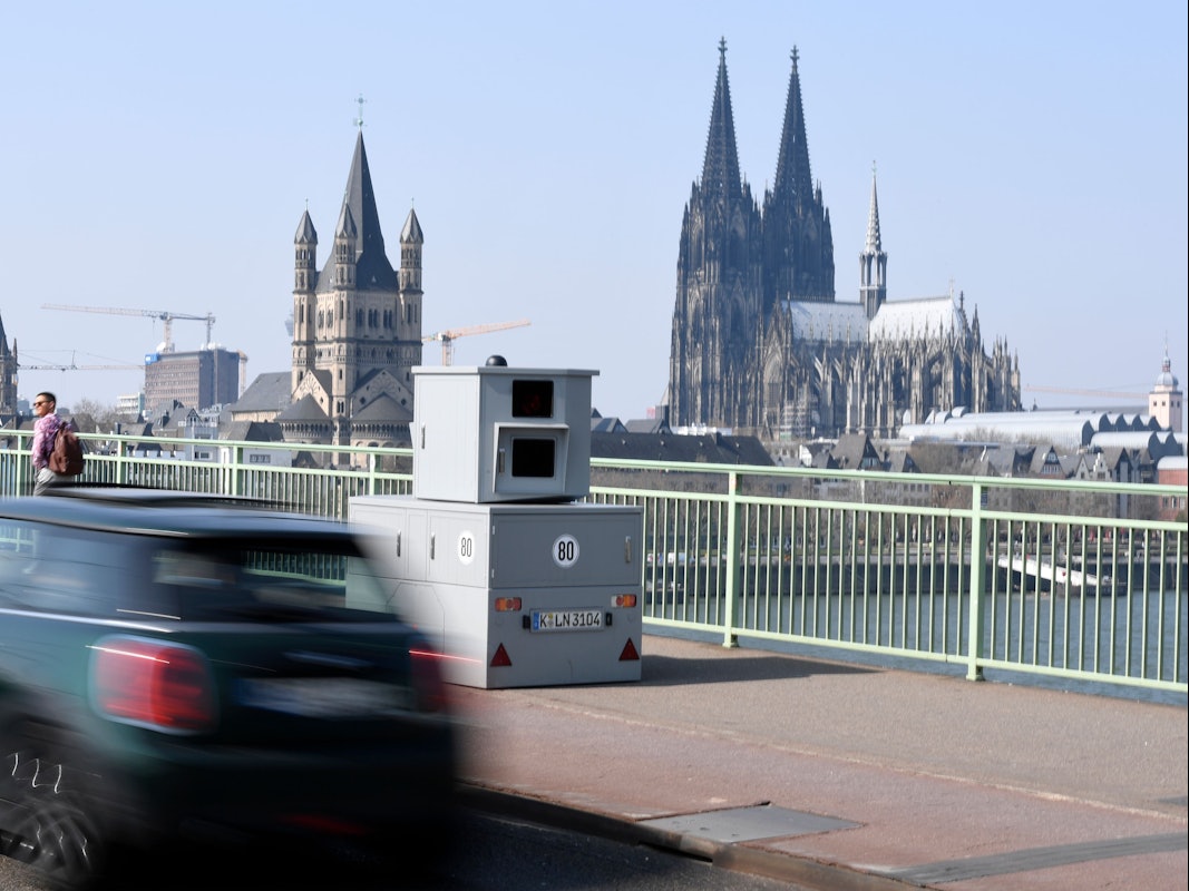 Ein Auto fährt an einem mobilen Blitzer vorbei, der mitten auf der Deutzer Brücke steht.