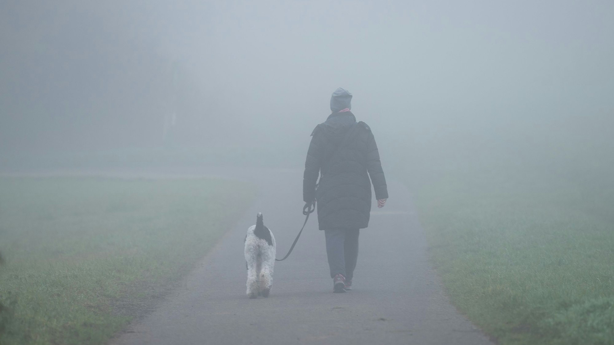 Ein Mann geht mit einem Hund im Nebel spazieren. Das Bild wurde am 21. November 2021 aufgenommen.