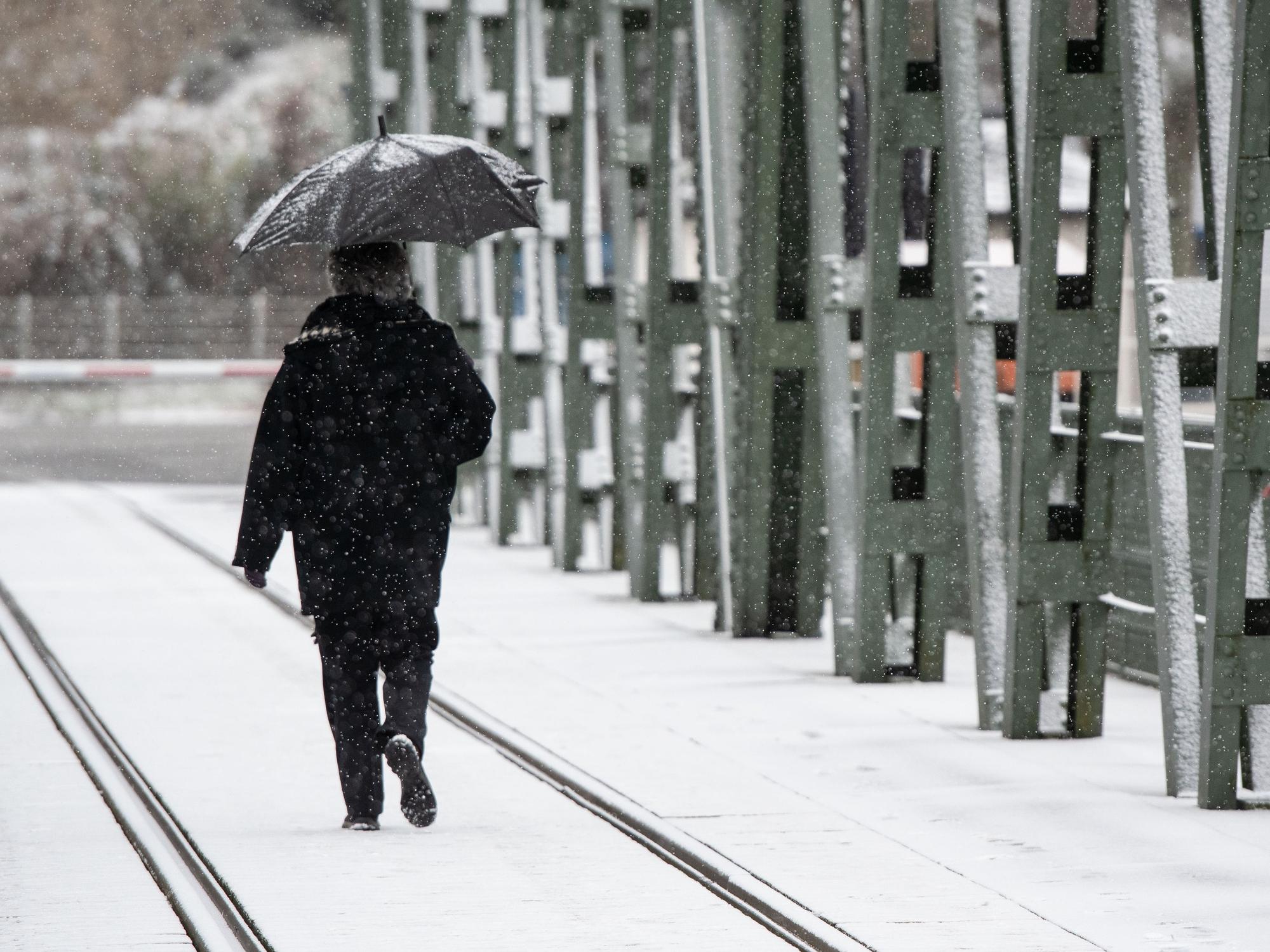 Eine Spaziergängerin mit einem Regenschirm geht bei leichtem Schneefall über eine Brücke am Hengsteysee.