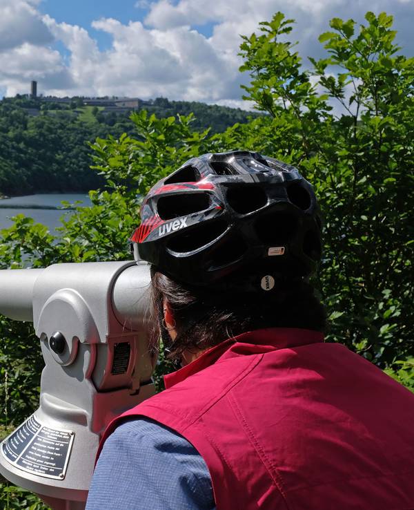 Das Foto vom 16. Juni 2019 zeigt eine Frau mit Fahrradhelm, die am Urftsee im Nationalpark Eifel durch ein Fernrohr blickt.