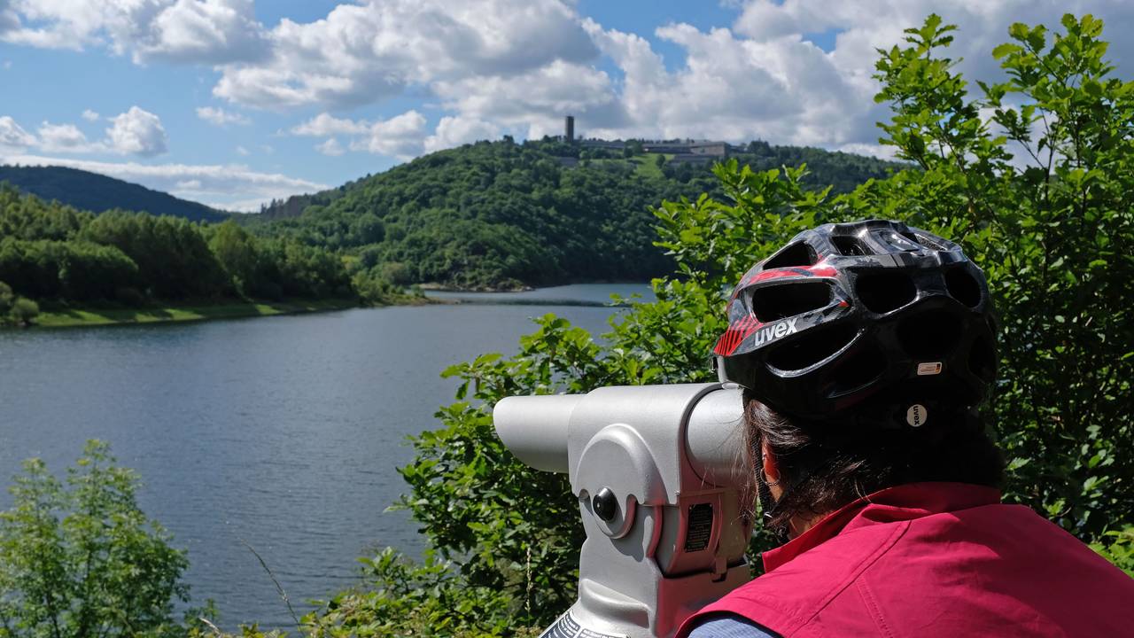 Das Foto vom 16. Juni 2019 zeigt eine Frau mit Fahrradhelm, die am Urftsee im Nationalpark Eifel durch ein Fernrohr blickt.