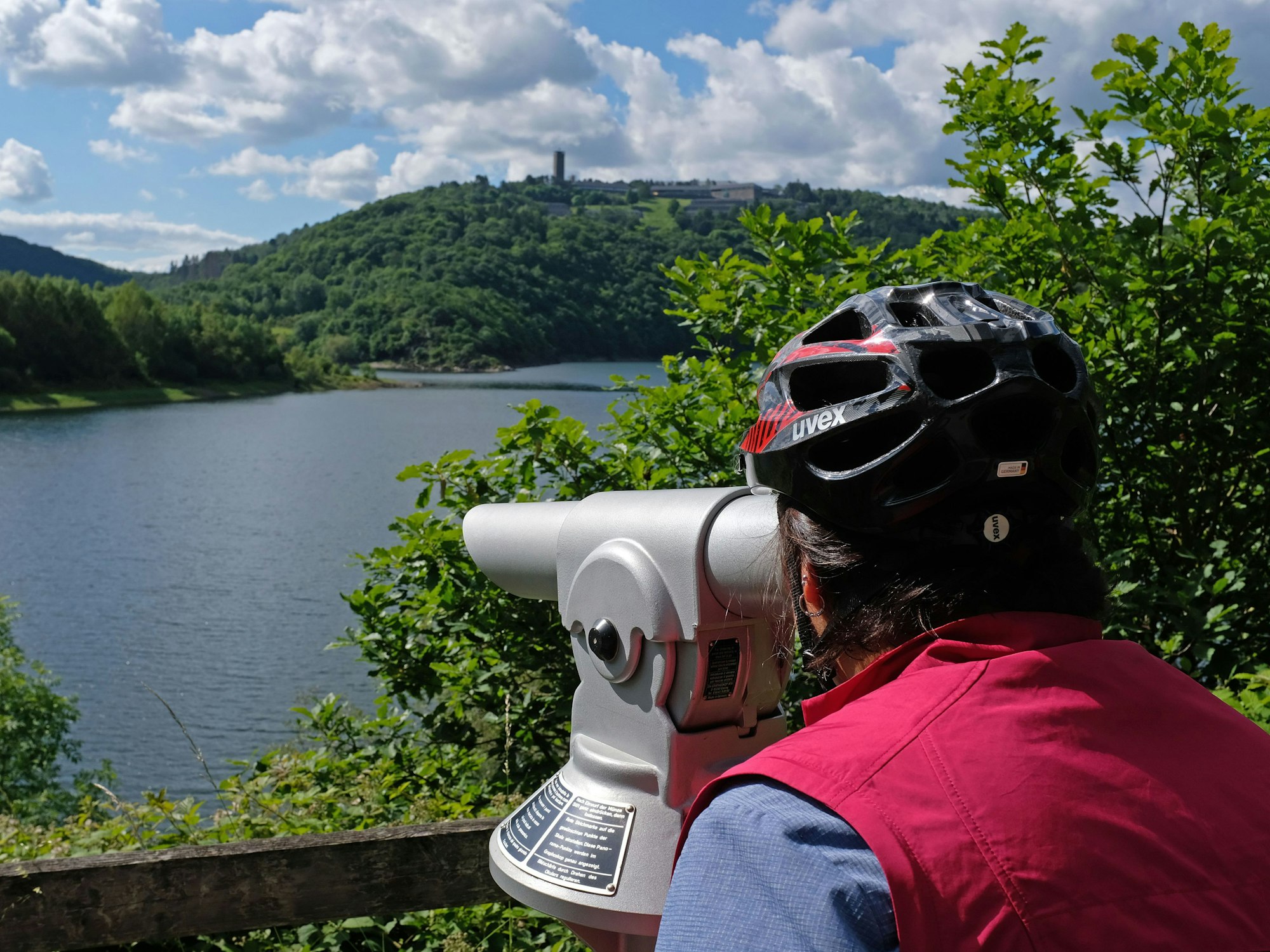 Das Foto vom 16. Juni 2019 zeigt eine Frau mit Fahrradhelm, die am Urftsee im Nationalpark Eifel durch ein Fernrohr blickt.