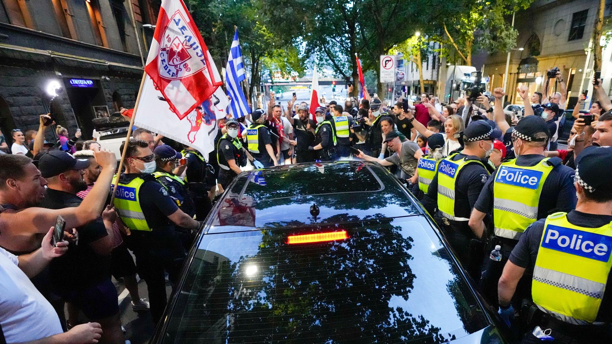 Anhänger des serbischen Tennisspielers Novak Djokovic stehen um ein von der Polizei umringtes Fahrzeug, das das Büro eines Anwalts verlässt.