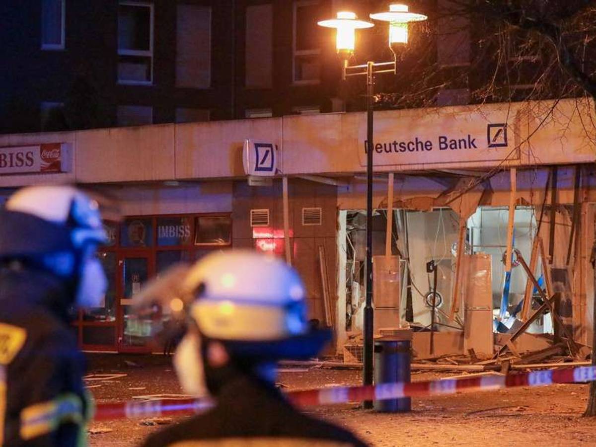 Einsatzkräfte der Feuerwehr stehen vor einer durch eine Explosion stark beschädigten Deutsche Bank-Filiale.