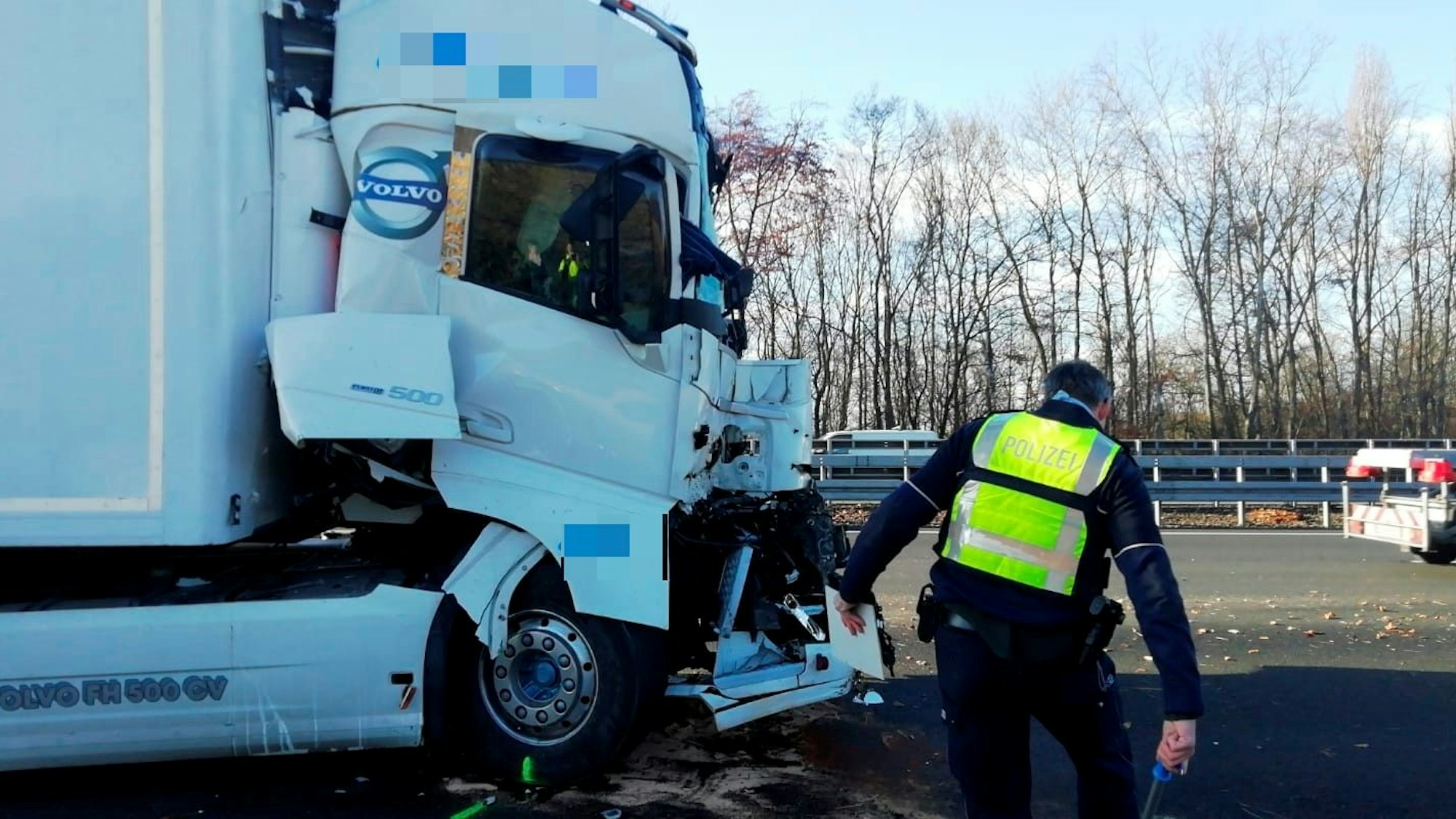 Die Front eines Lkw ist stark beschädigt, ein Polizist guckt sich den Schaden an.