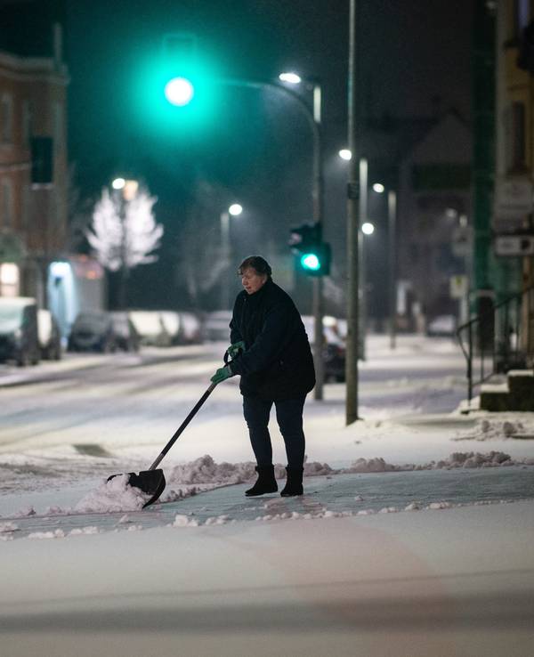 Eine Frau schippt am frühen Morgen Schnee auf dem Bürgersteig.