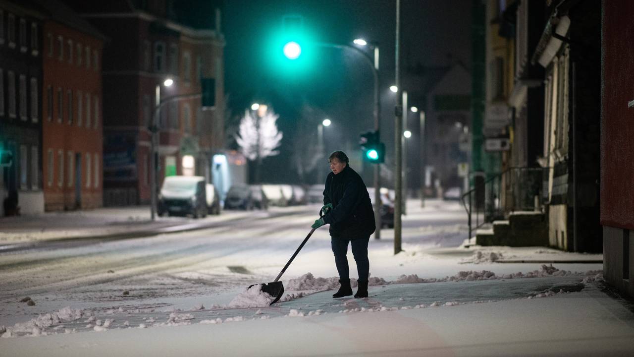 Eine Frau schippt am frühen Morgen Schnee auf dem Bürgersteig.
