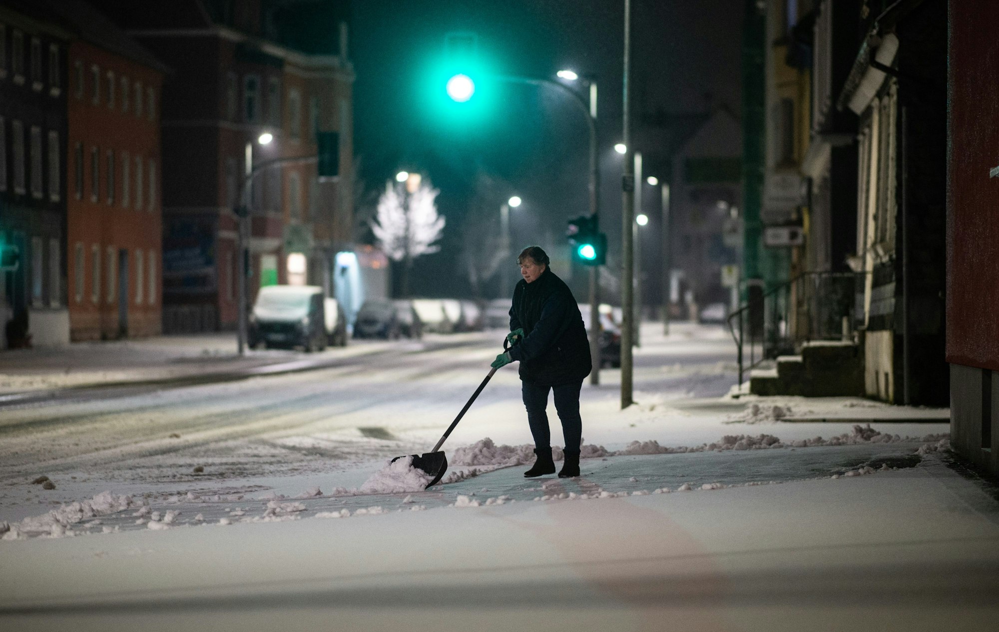 Eine Frau schippt am frühen Morgen Schnee auf dem Bürgersteig.