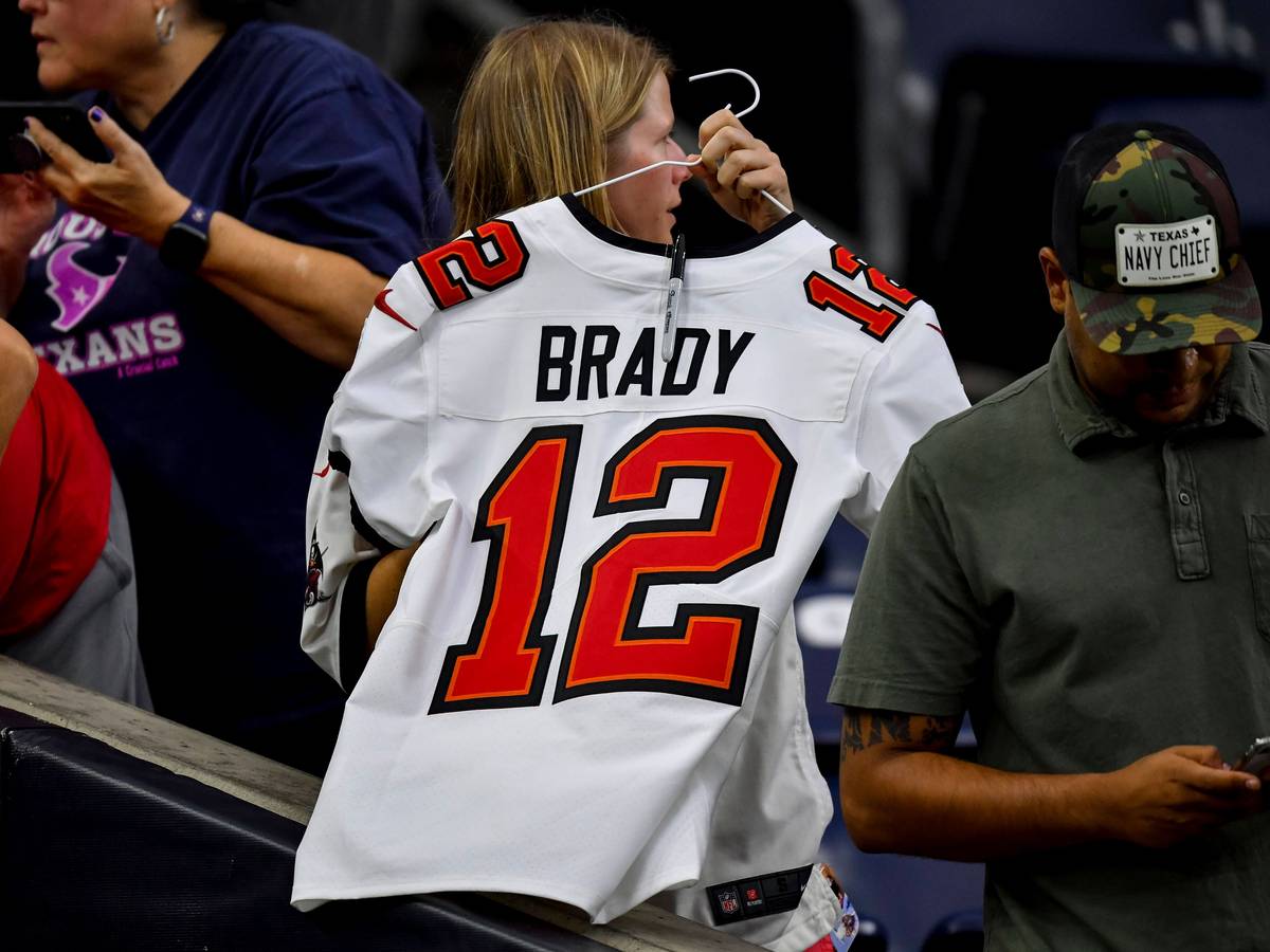 Ein Frau hält einen Kleiderbügel in den Händen. Daran hängt ein weißes Trikot von Tom Brady mit der Nummer 12.