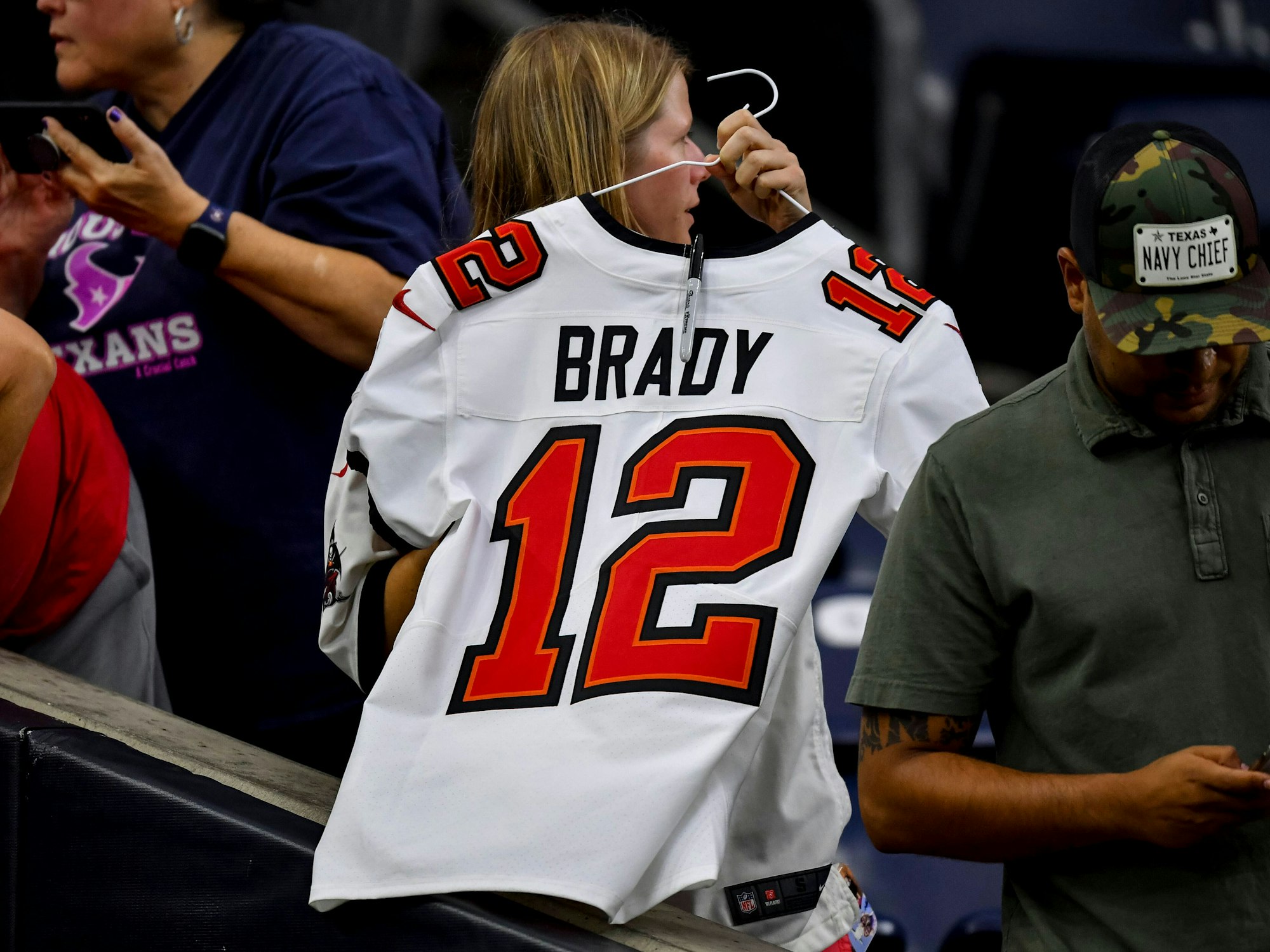 Ein Frau hält einen Kleiderbügel in den Händen. Daran hängt ein weißes Trikot von Tom Brady mit der Nummer 12.