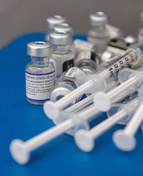 Spritzen und Fläschchen mit dem Impfstoff COVID-19 von Pfizer-BioNTech liegen auf einer Arbeitsfläche.