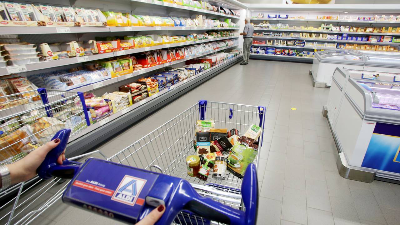 Eine Person schiebt einen befüllten Einkaufswagen durch eine Aldi Nord Filiale.