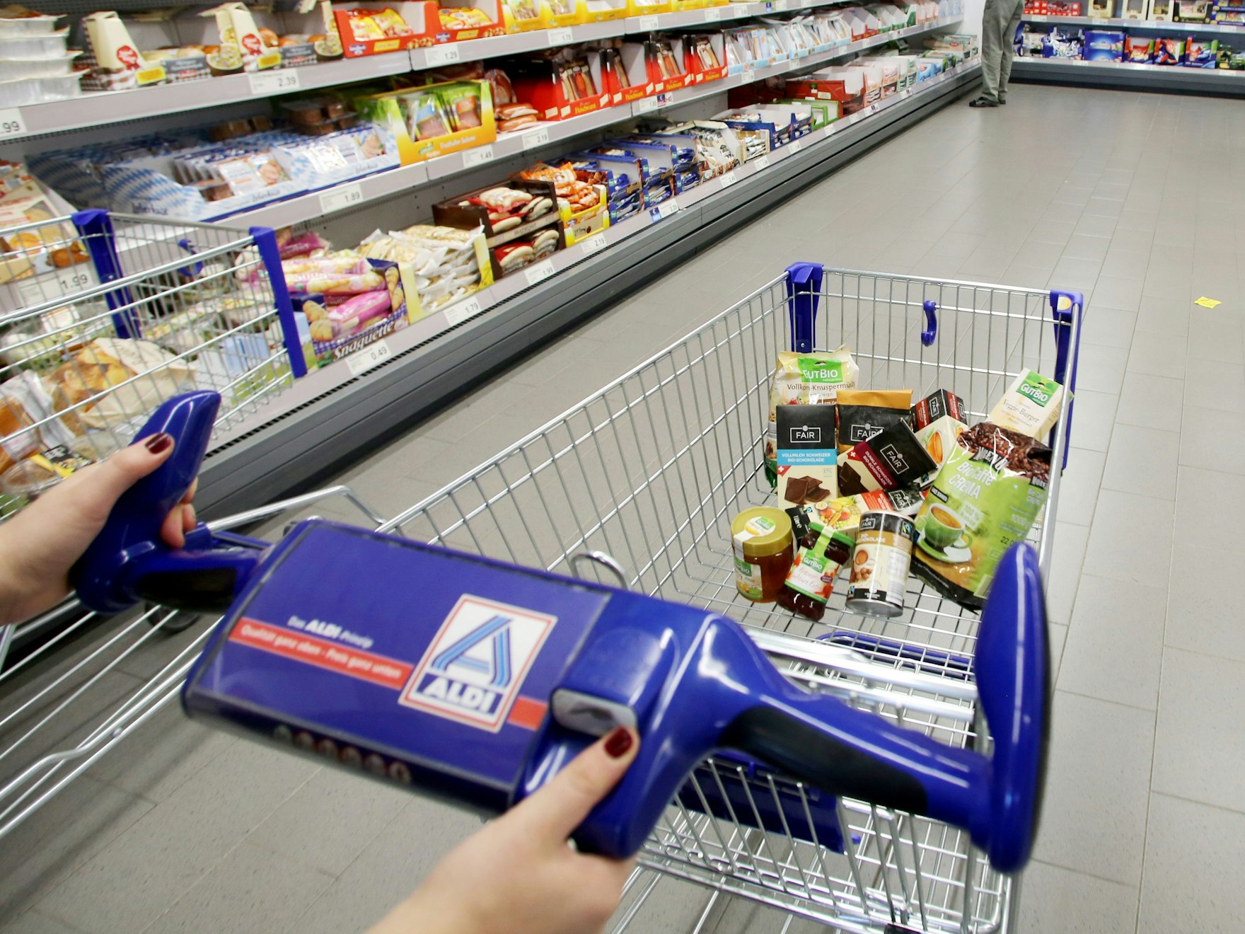 Eine Person schiebt einen befüllten Einkaufswagen durch eine Aldi Nord Filiale.