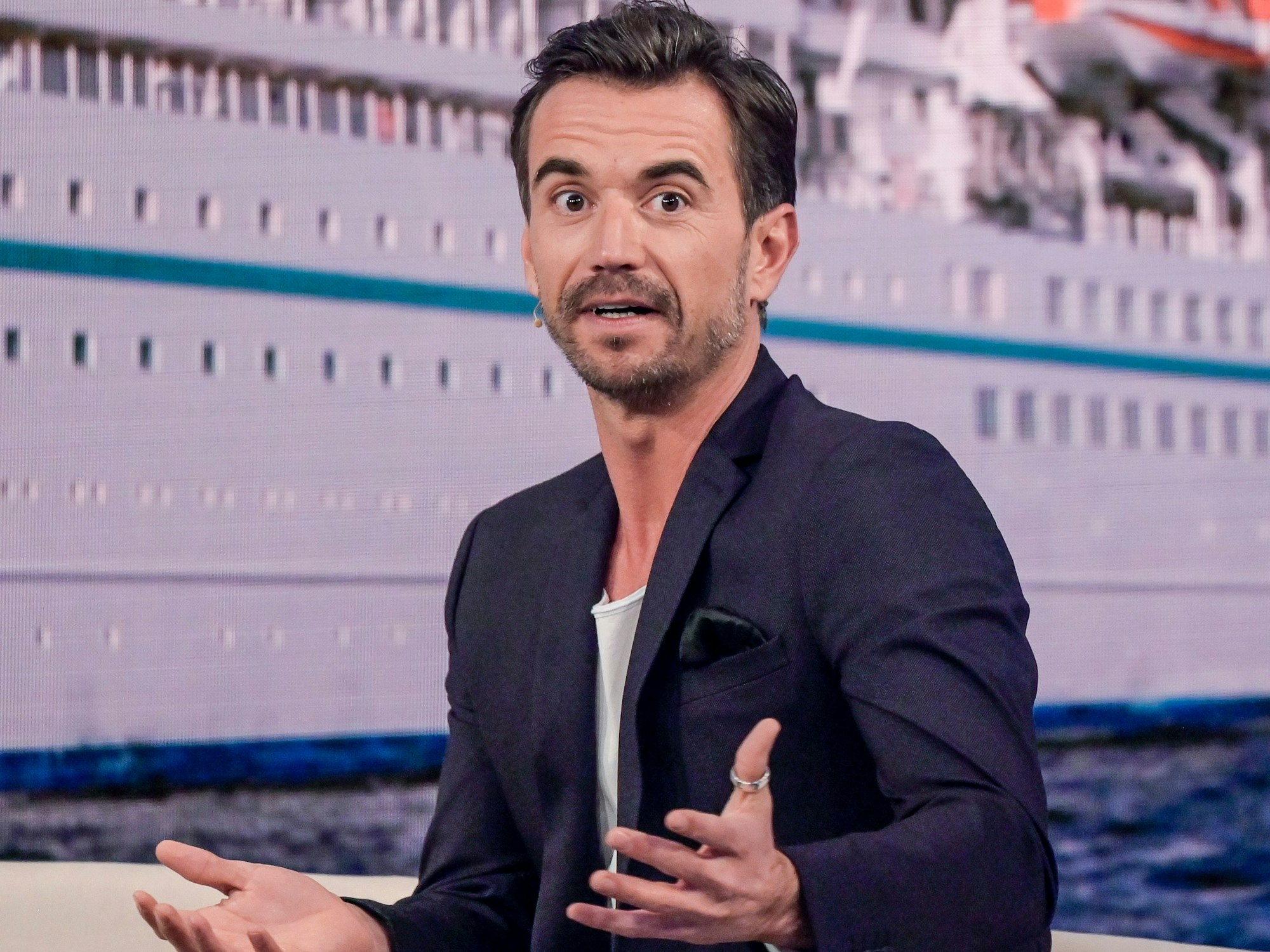 Der Moderator Florian Silbereisen sitzt bei der Aufzeichnung des großen Jahresrückblicks „Menschen 2019“ auf der Bühne. Im Hintergrund ist das ZDF-„Traumschiff“ zu sehen.
