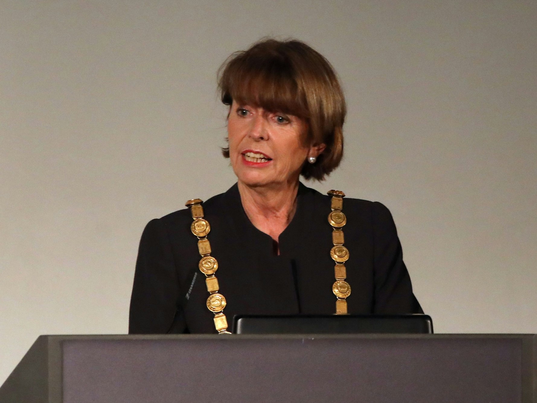 Henriette Reker spricht mit OB-Kette an einem Pult.