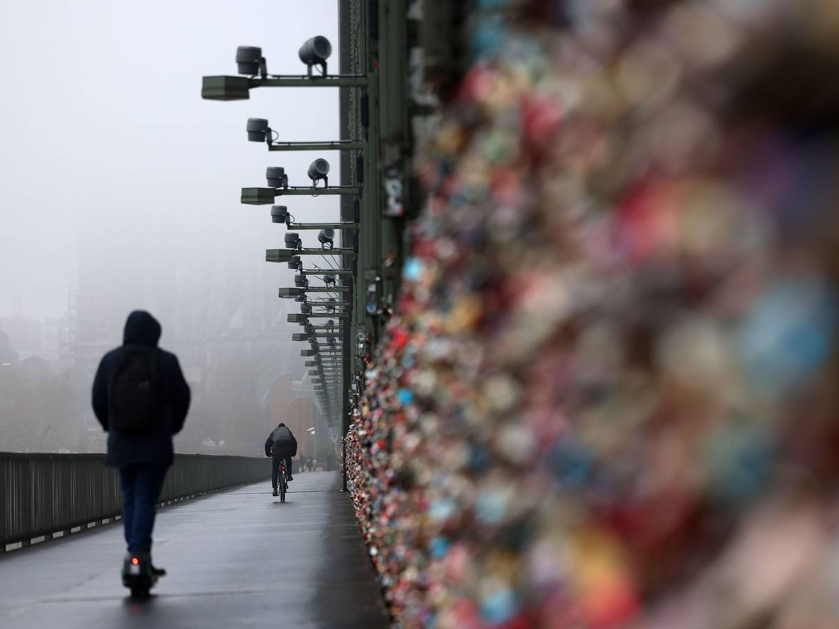 Ein E-Scooter Fahrer fährt über die Hohenzollernbrücke, der Dom im Hintergrund ist im Nebel.