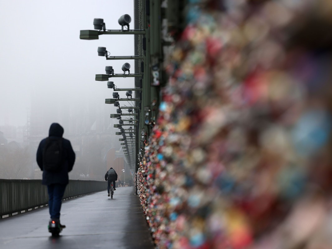 Ein E-Scooter Fahrer fährt über die Hohenzollernbrücke, der Dom im Hintergrund ist im Nebel.