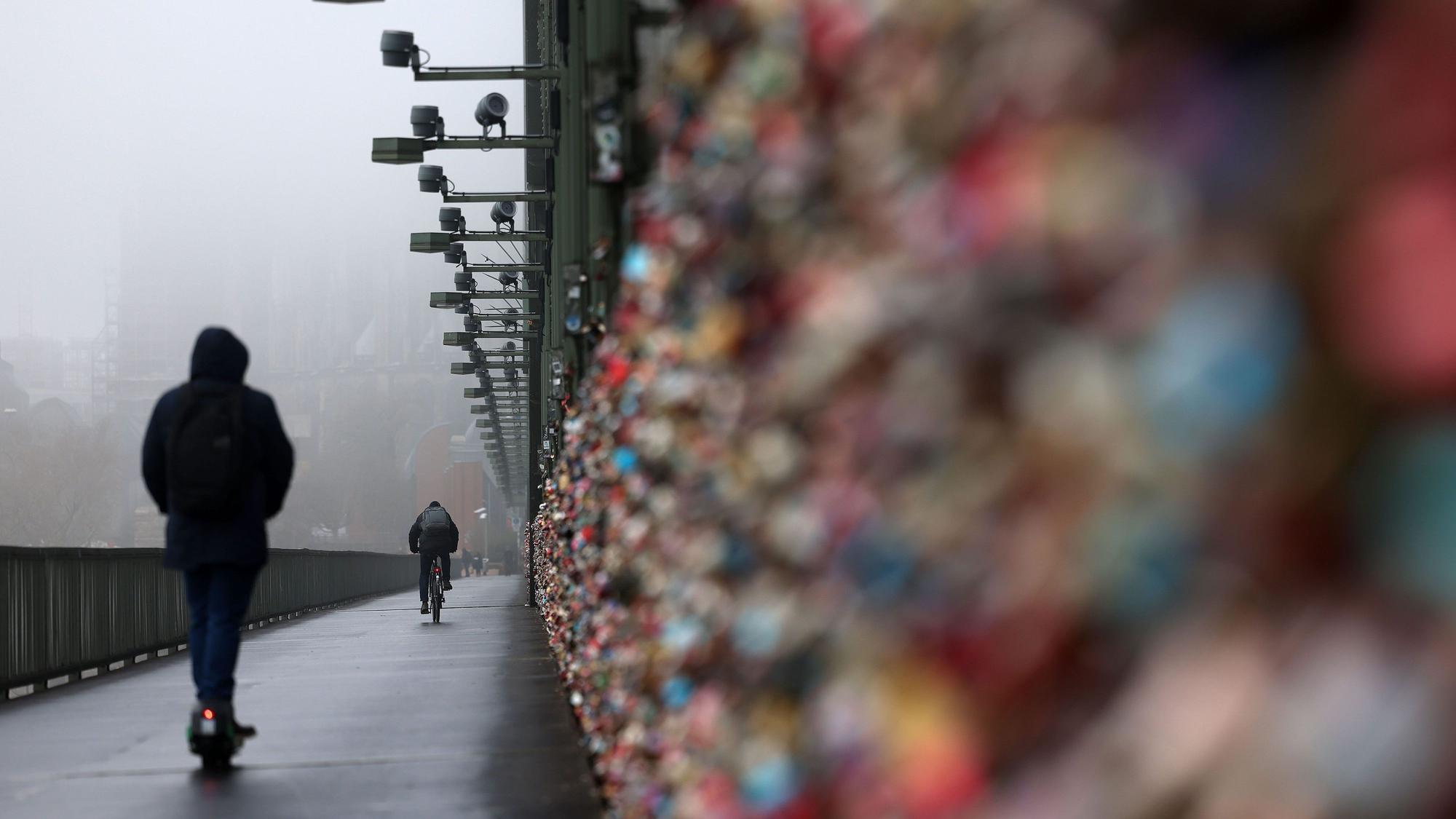 Ein E-Scooter Fahrer fährt über die Hohenzollernbrücke, der Dom im Hintergrund ist im Nebel.