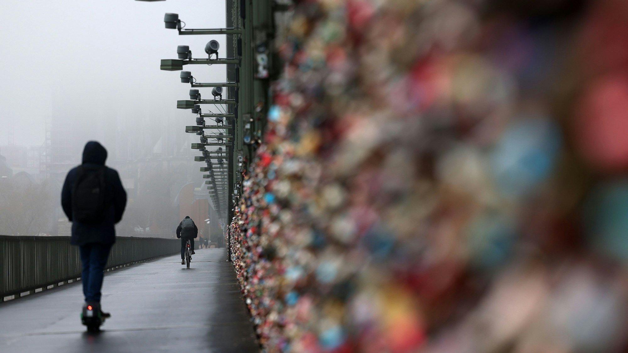 Ein E-Scooter Fahrer fährt über die Hohenzollernbrücke, der Dom im Hintergrund ist im Nebel.