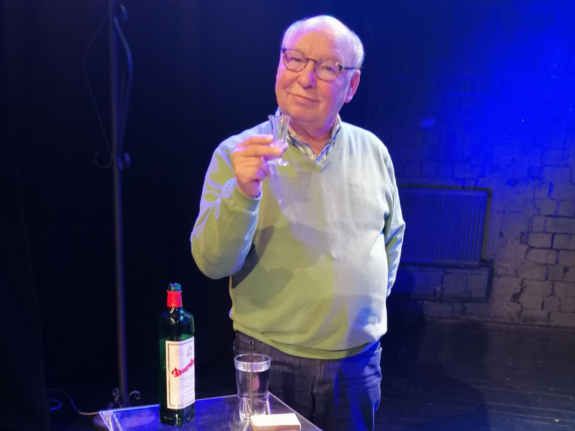 Hans-Joachim Heist hält ein kleines Glas hoch und lächelt in die Kamera.