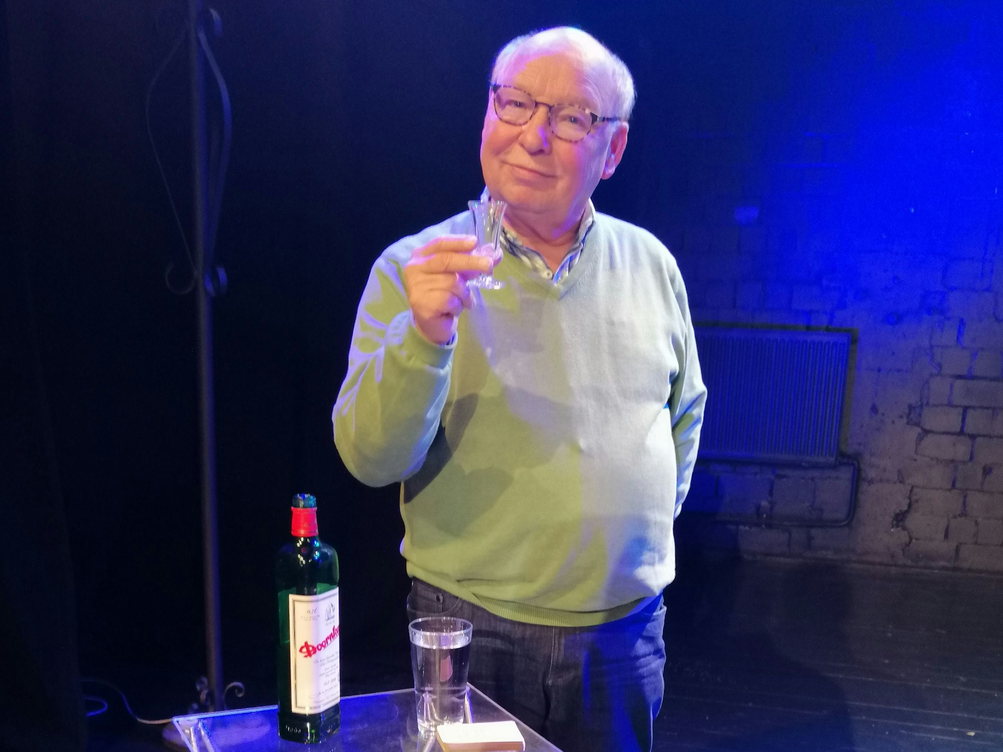 Hans-Joachim Heist hält ein kleines Glas hoch und lächelt in die Kamera.