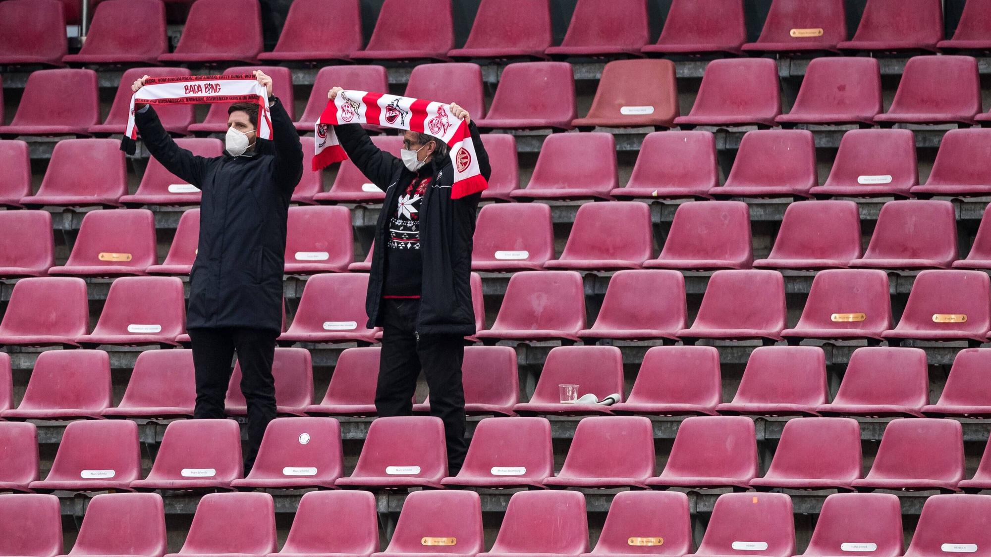 Zwei Fans des 1. FC Köln stehen auf der Tribüne und halten ihre Schals in die Höhe