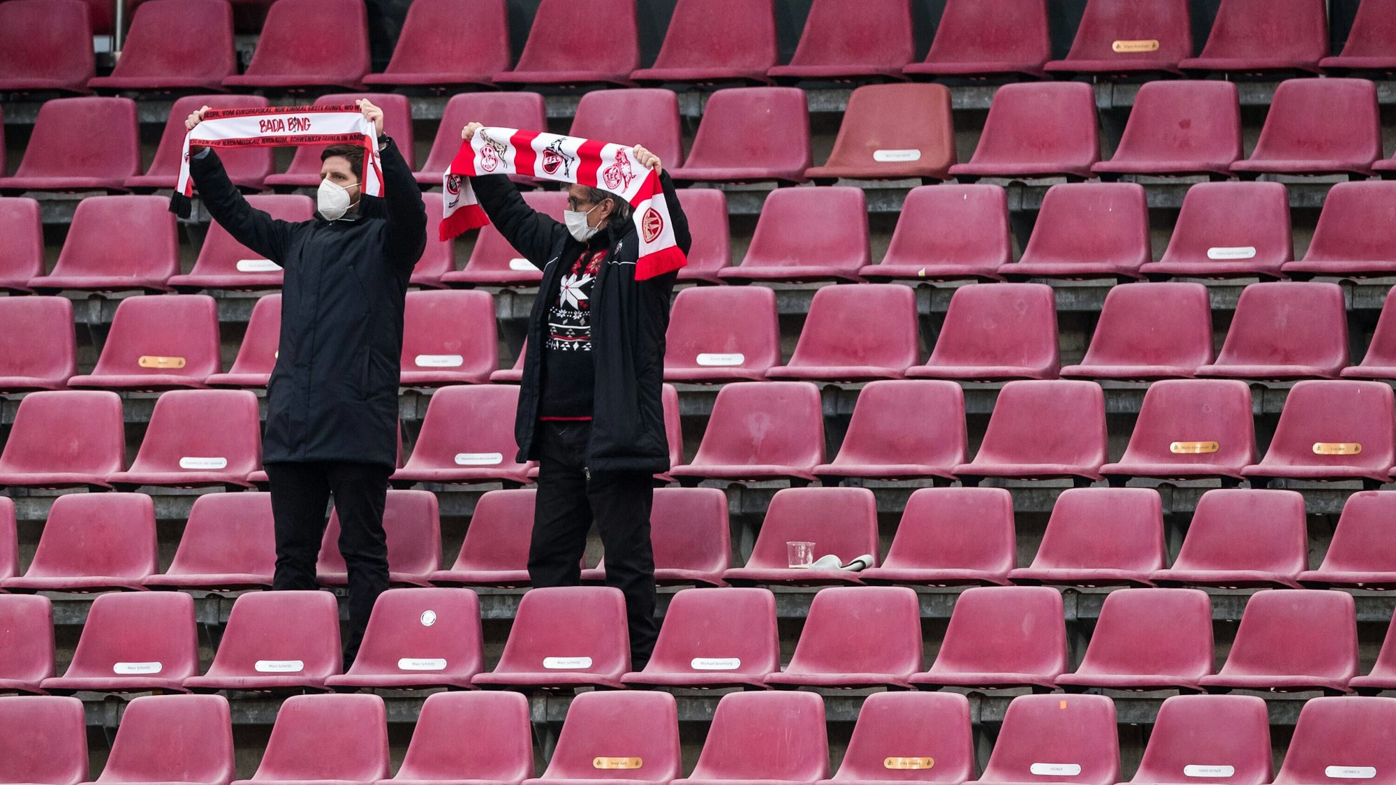 Zwei Fans des 1. FC Köln stehen auf der Tribüne und halten ihre Schals in die Höhe
