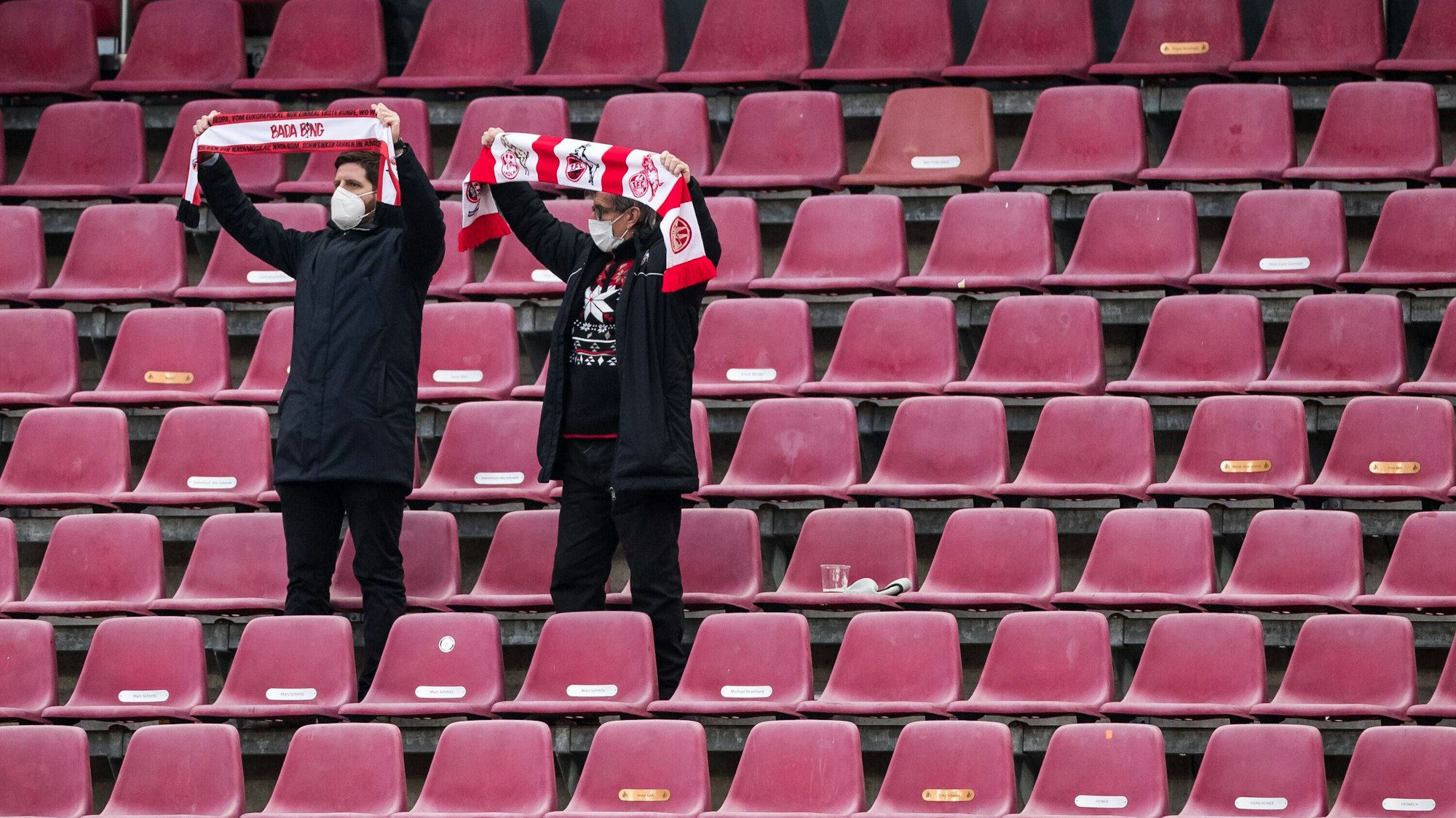 Zwei Fans des 1. FC Köln stehen auf der Tribüne und halten ihre Schals in die Höhe