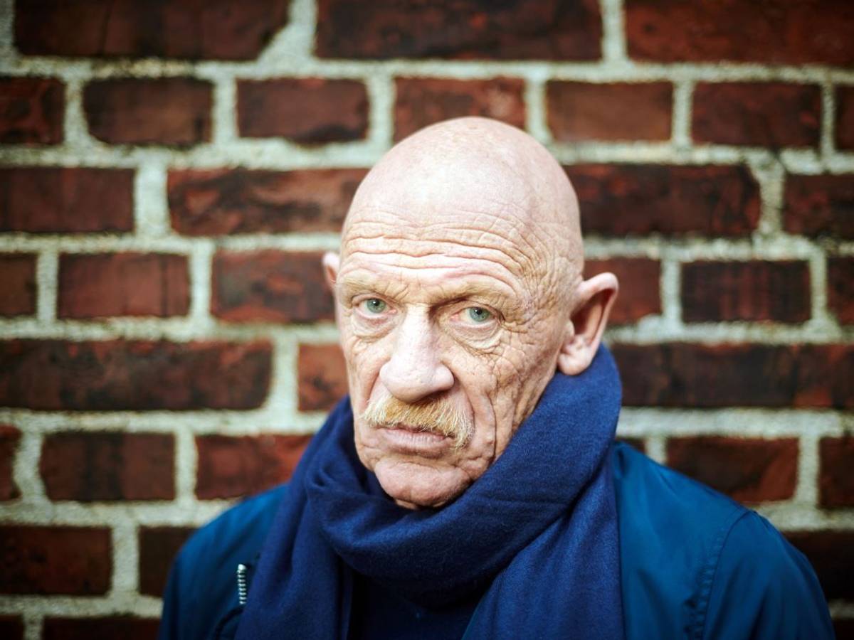 Schauspieler Joe Bausch steht vor einer Mauer und schaut in die Kamera.
