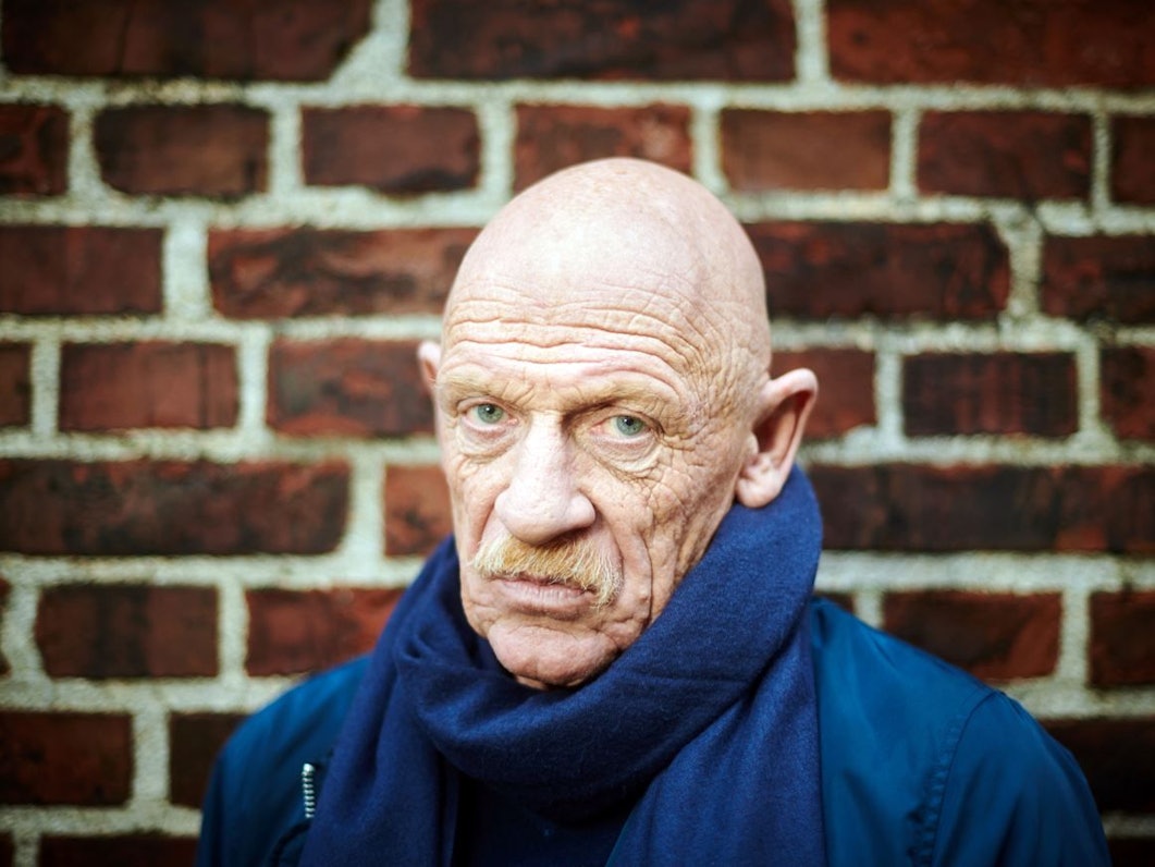 Schauspieler Joe Bausch steht vor einer Mauer und schaut in die Kamera.