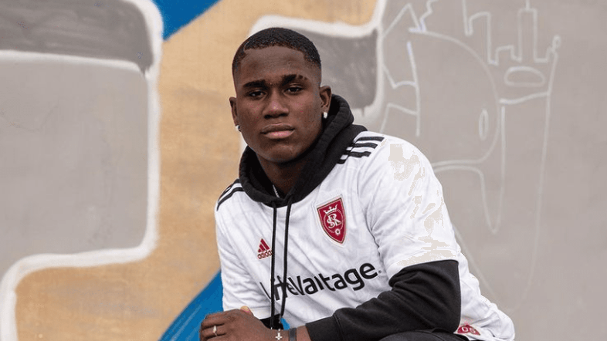 Axel Kei kniet vor einer Wand und trägt ein weißes Trikot von Real Salt Lake.