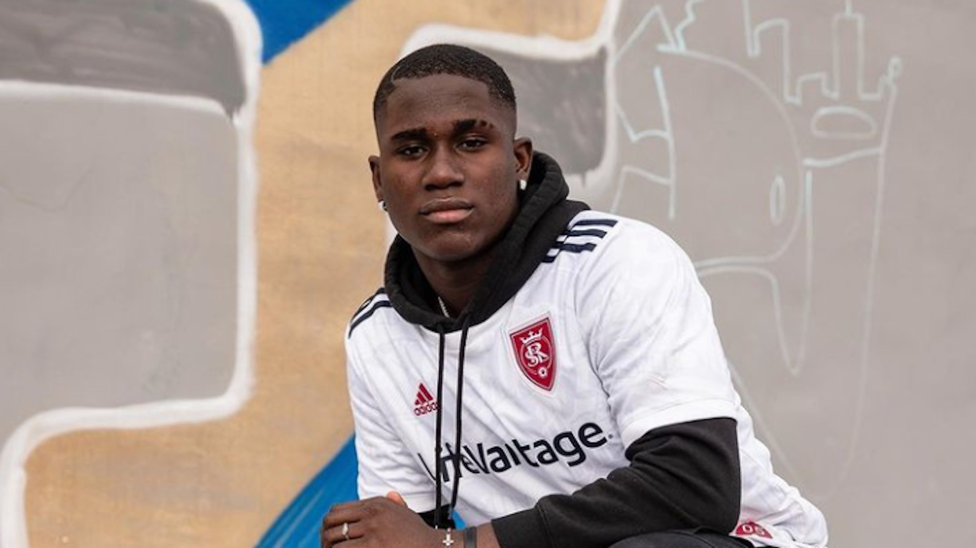 Axel Kei kniet vor einer Wand und trägt ein weißes Trikot von Real Salt Lake.