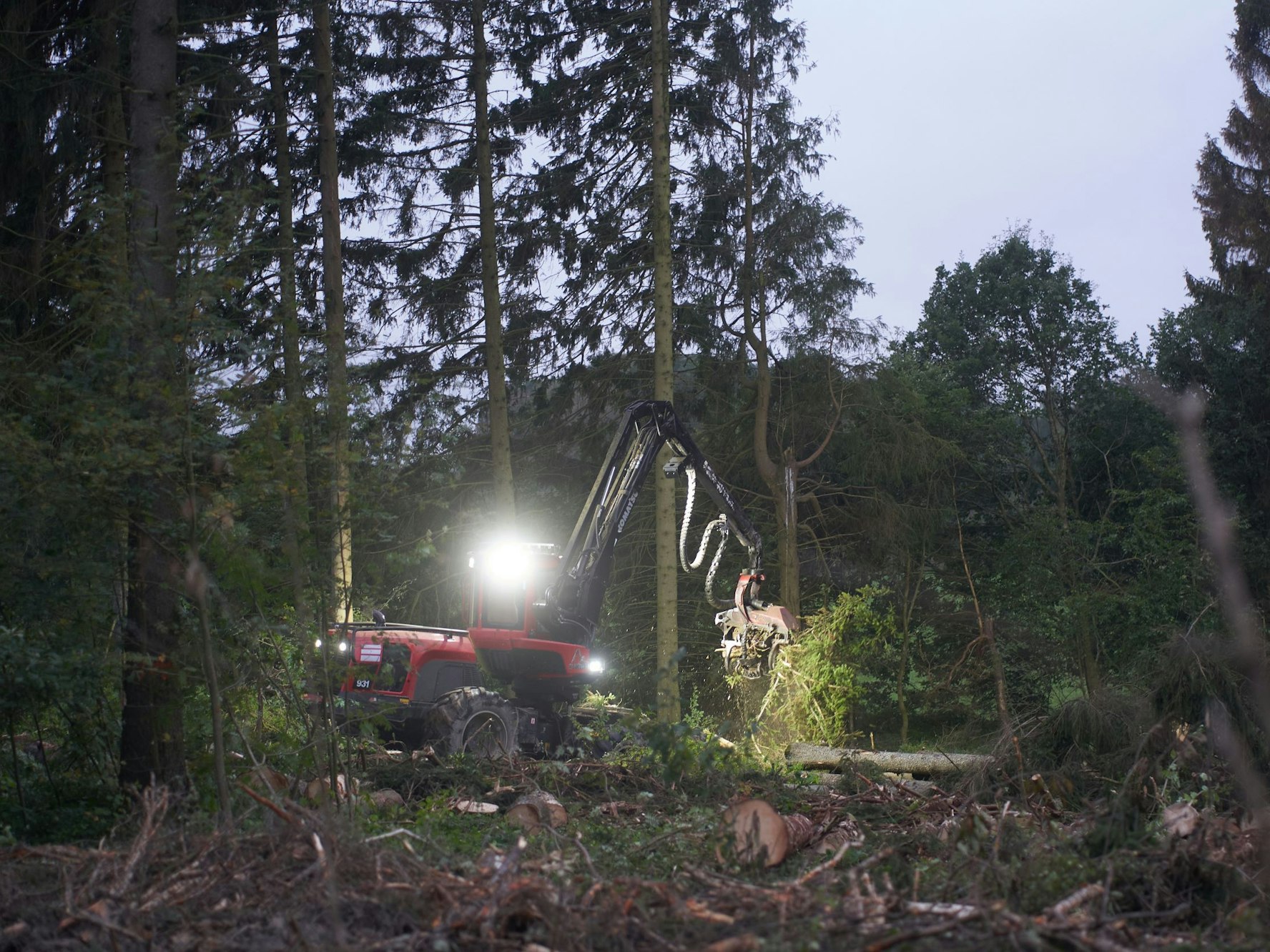 Ein Harvester erntet am Waldrand in der Eifel bei Döttingen im Schein seiner Scheinwerfer an einem bedeckten Morgen Holz.