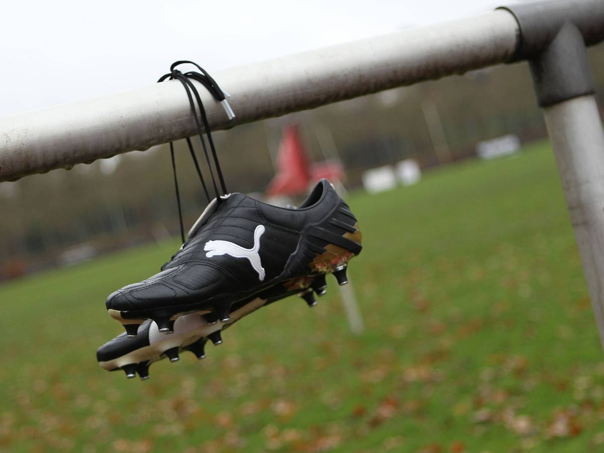 Fußballschuhe von Puma hängen an der Balustrade eines geschlossenen Sportplatzes.
