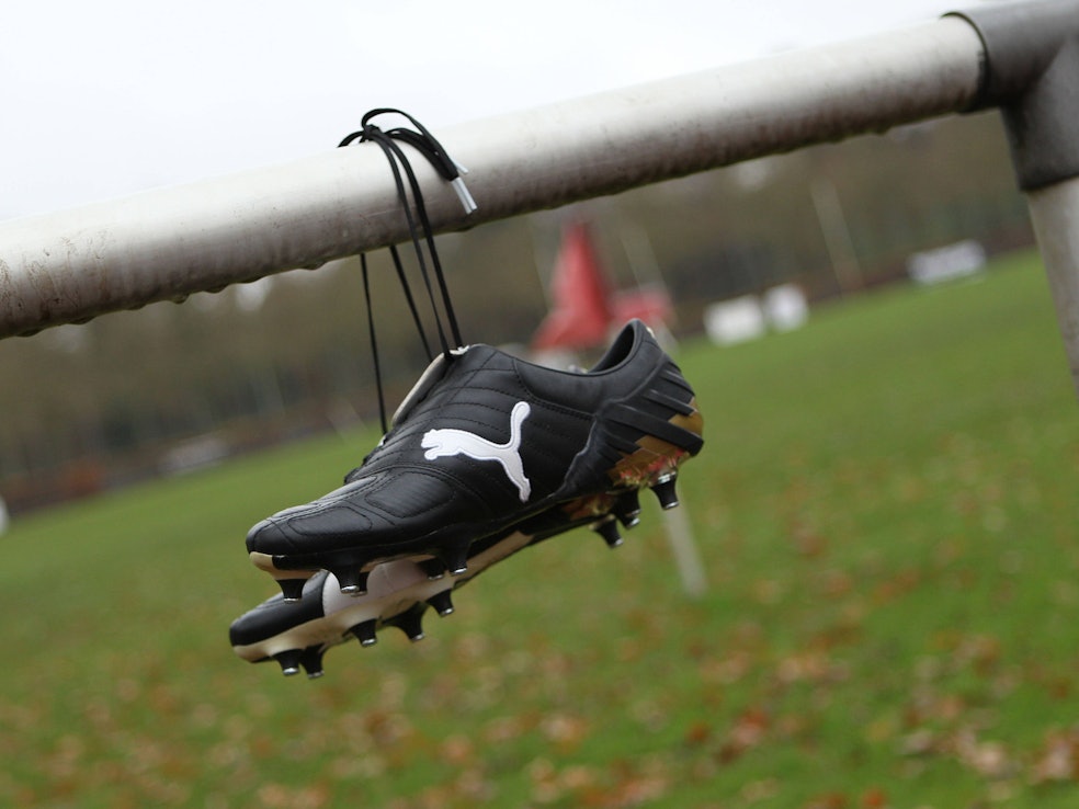 Fußballschuhe von Puma hängen an der Balustrade eines geschlossenen Sportplatzes.
