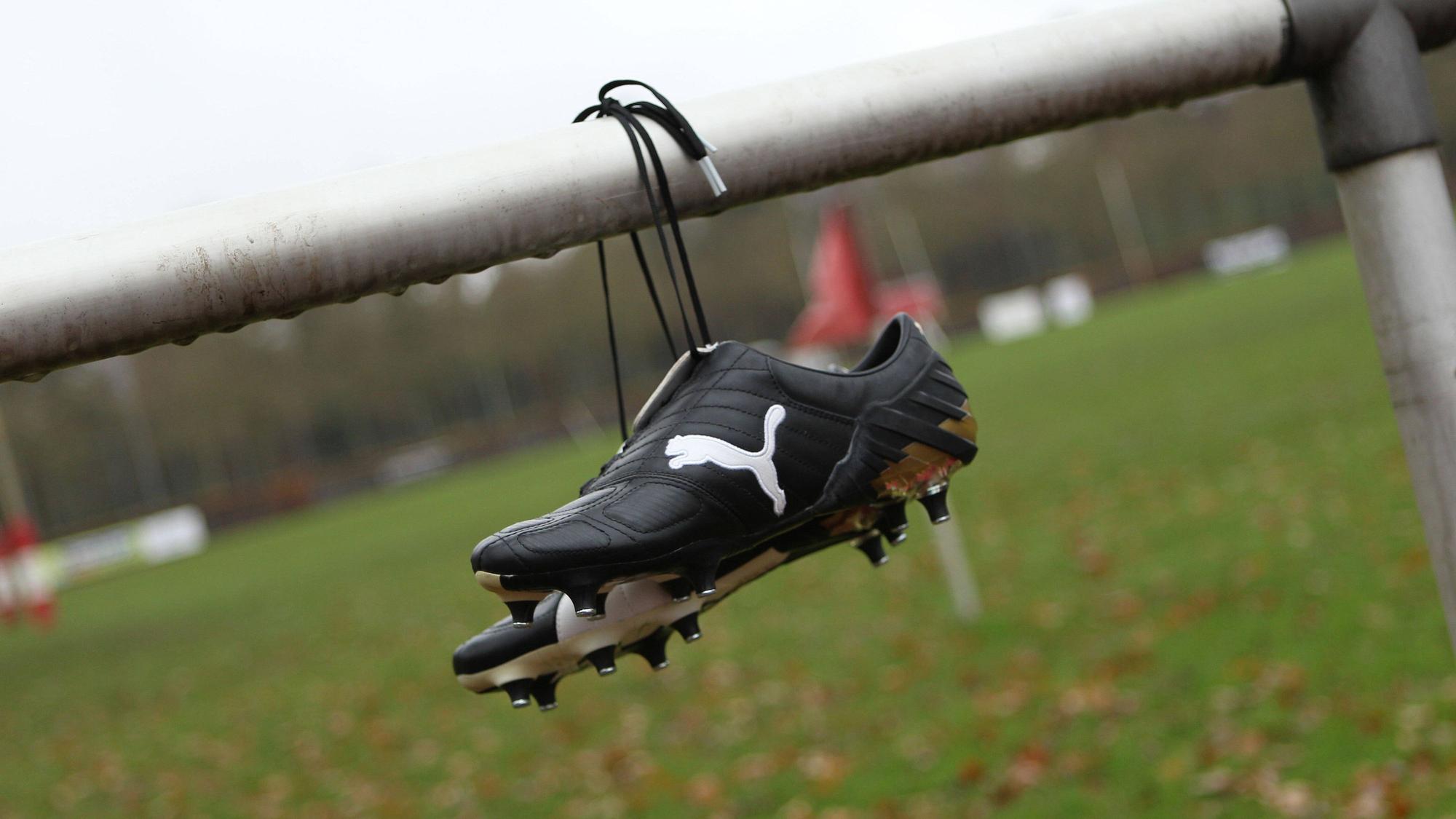 Fußballschuhe von Puma hängen an der Balustrade eines geschlossenen Sportplatzes.