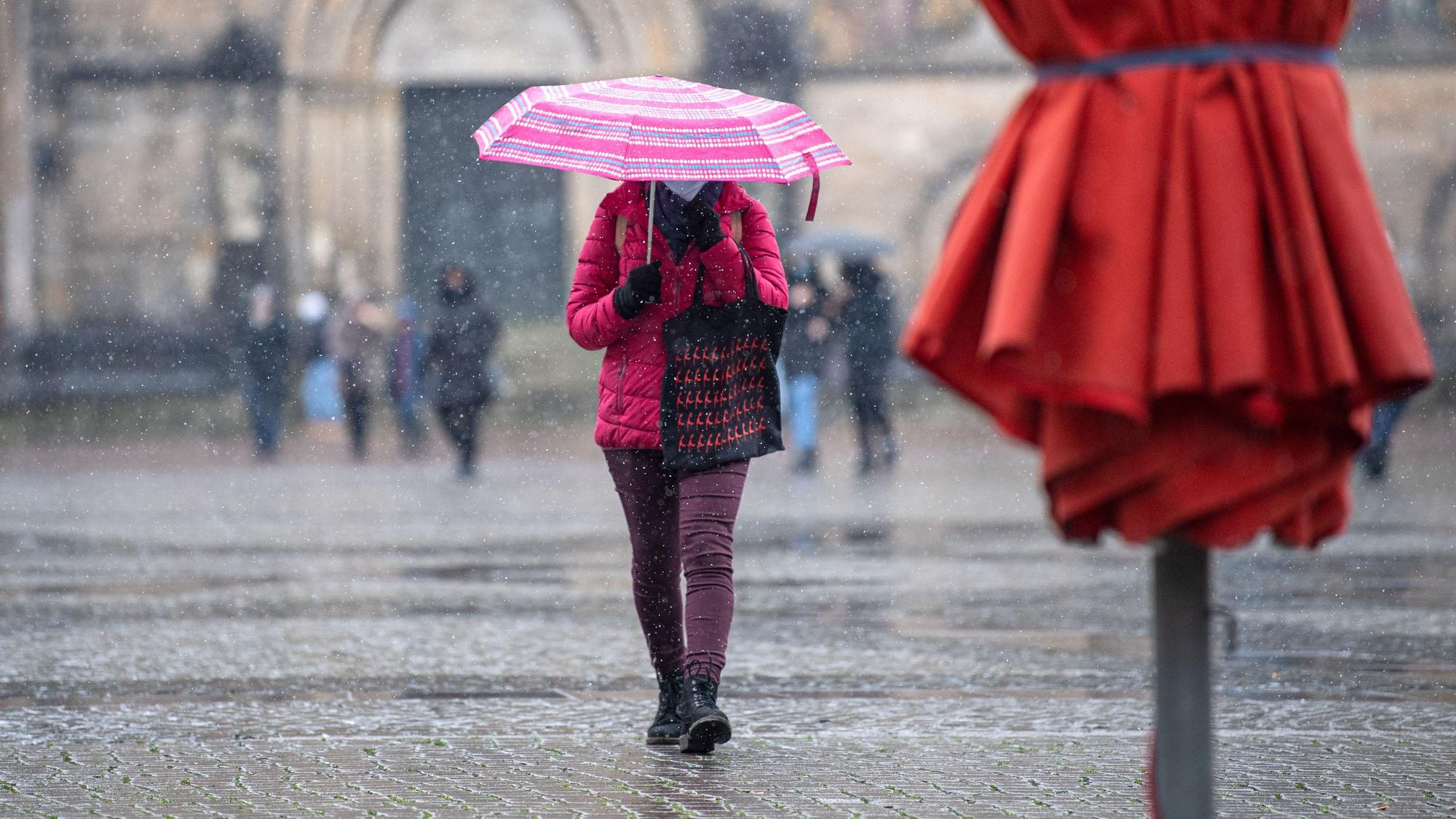 Eine Frau mit Regenschirm läuft bei Schneeregen über den Marktplatz.