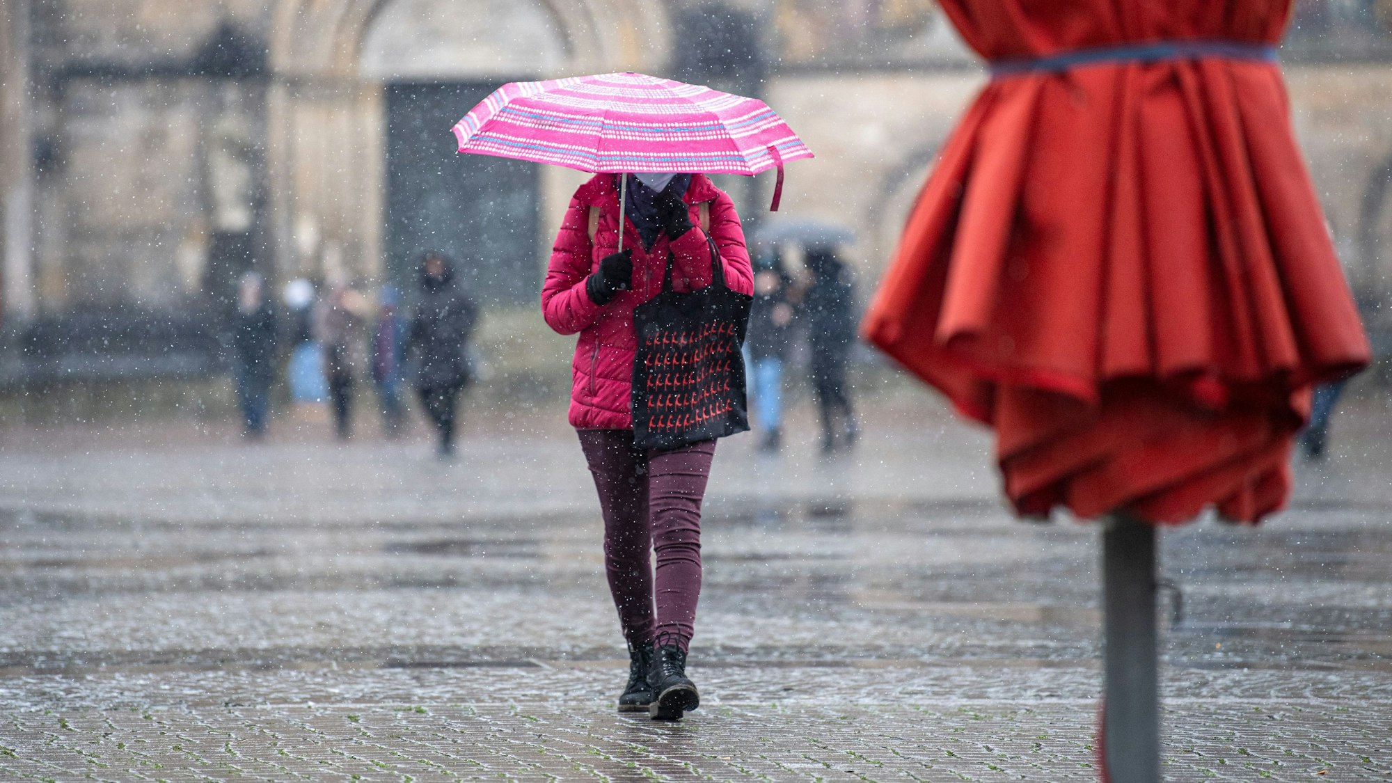 Eine Frau mit Regenschirm läuft bei Schneeregen über den Marktplatz.
