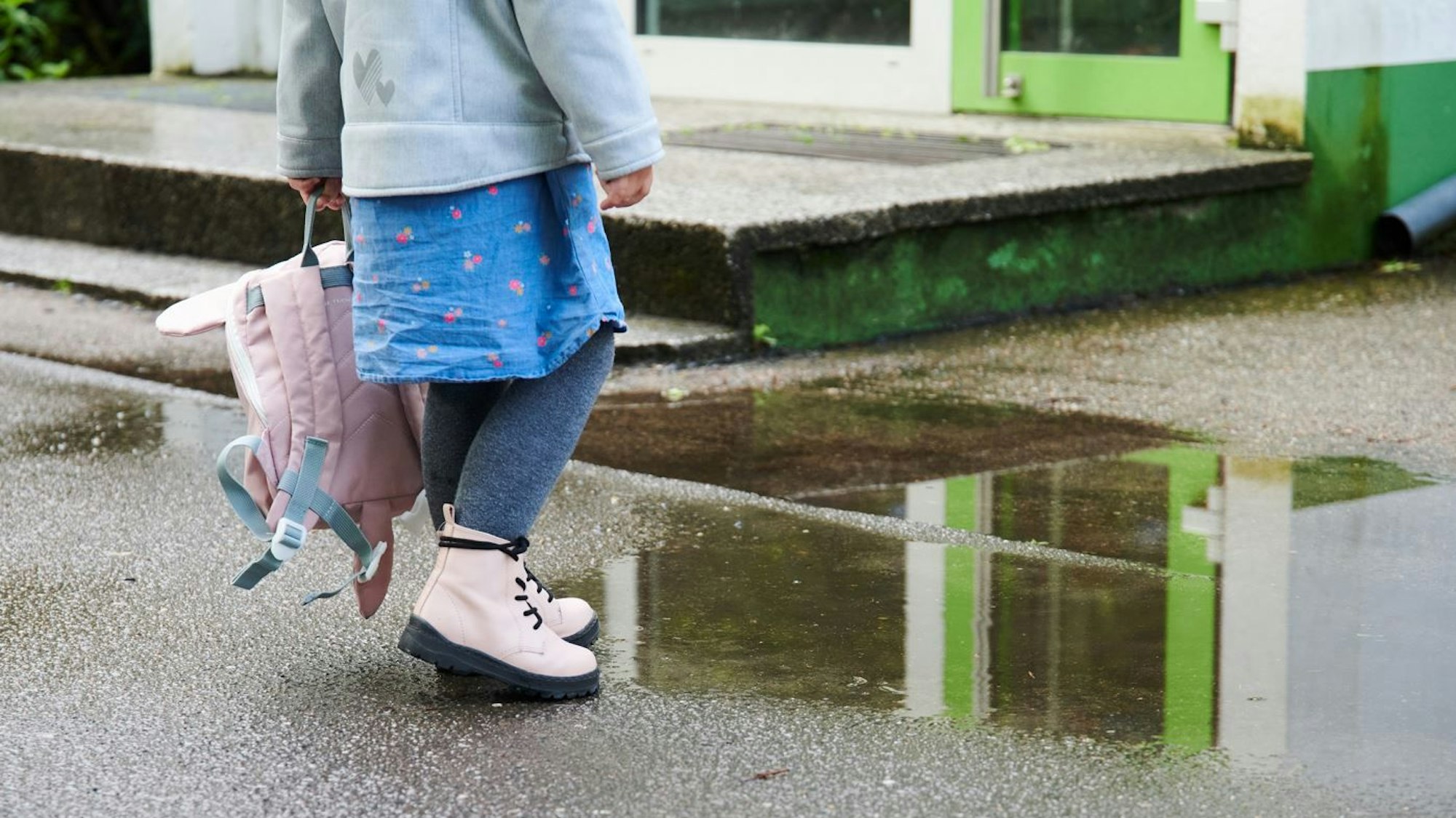 Berlin: Vor dem Eingang einer Kita spielt ein Kind an einer Pfütze.