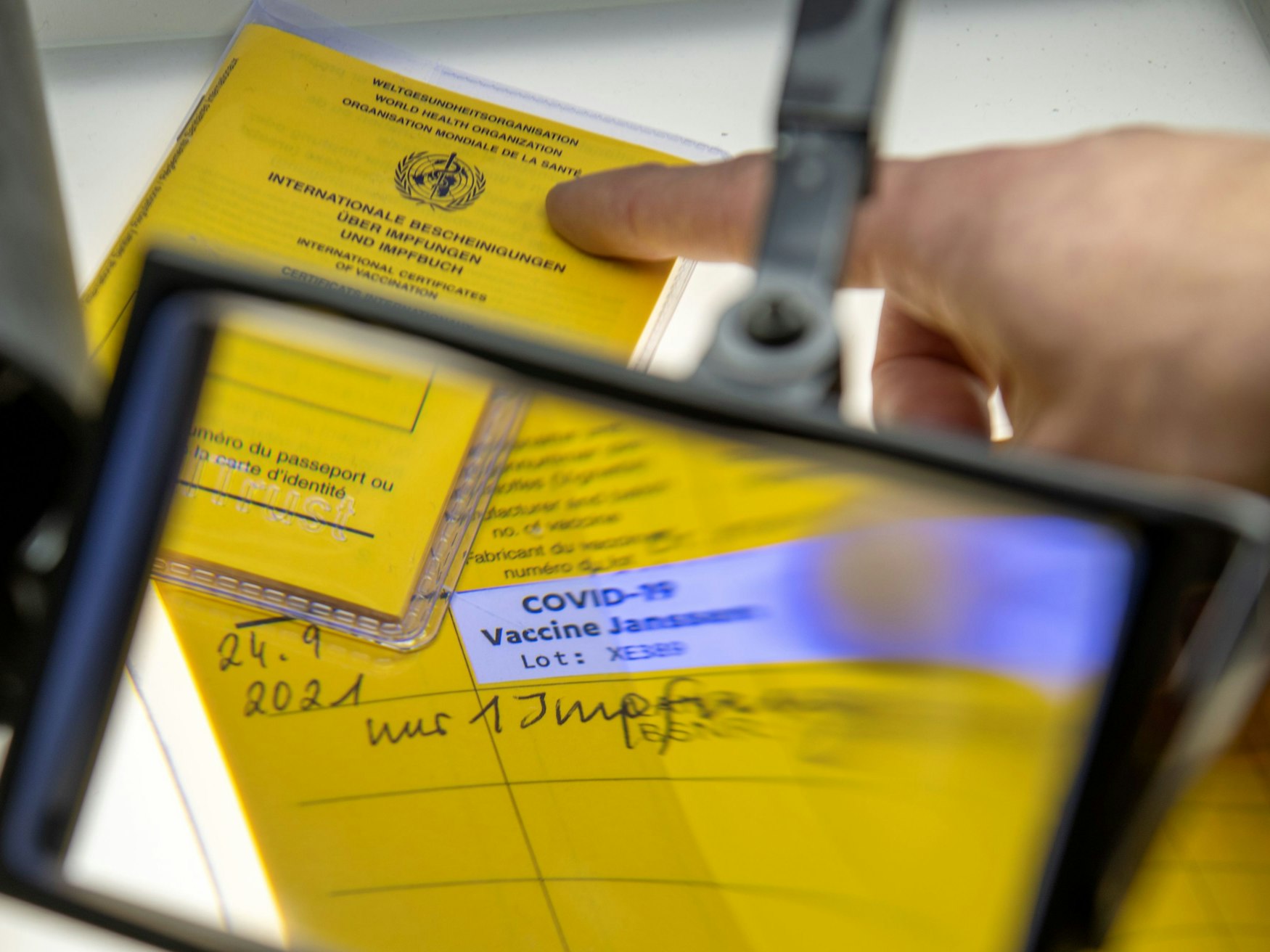 Bei der Kriminalpolizeiinspektion liegen Impfpässe unter einer Lupe, darunter ein aufgeschlagener Impfausweis mit einem Eintrag einer Corona-Impfung Corona-Impfung mit dem Impfstoff Johnson & Johnson.