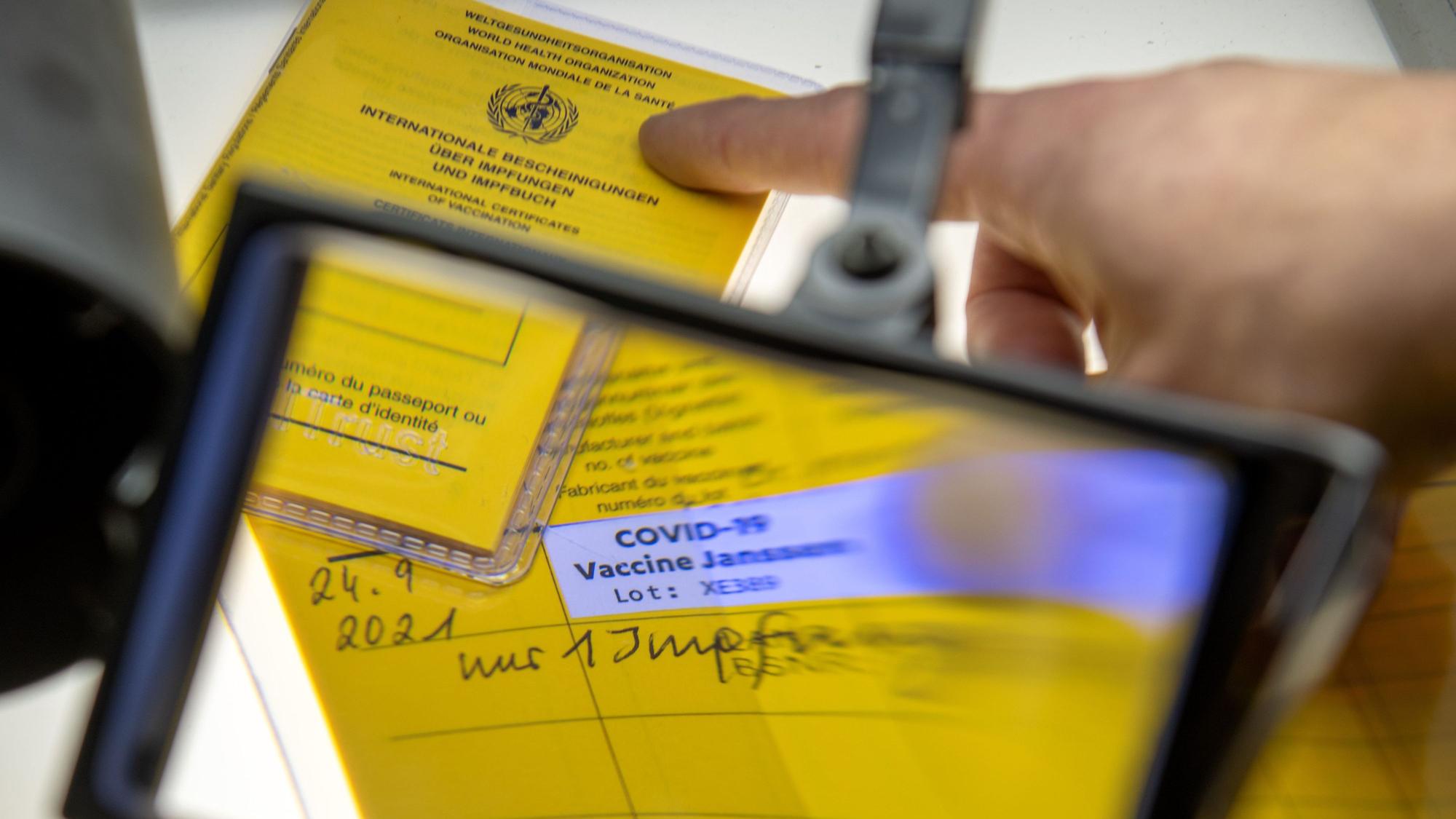 Bei der Kriminalpolizeiinspektion liegen Impfpässe unter einer Lupe, darunter ein aufgeschlagener Impfausweis mit einem Eintrag einer Corona-Impfung Corona-Impfung mit dem Impfstoff Johnson & Johnson.