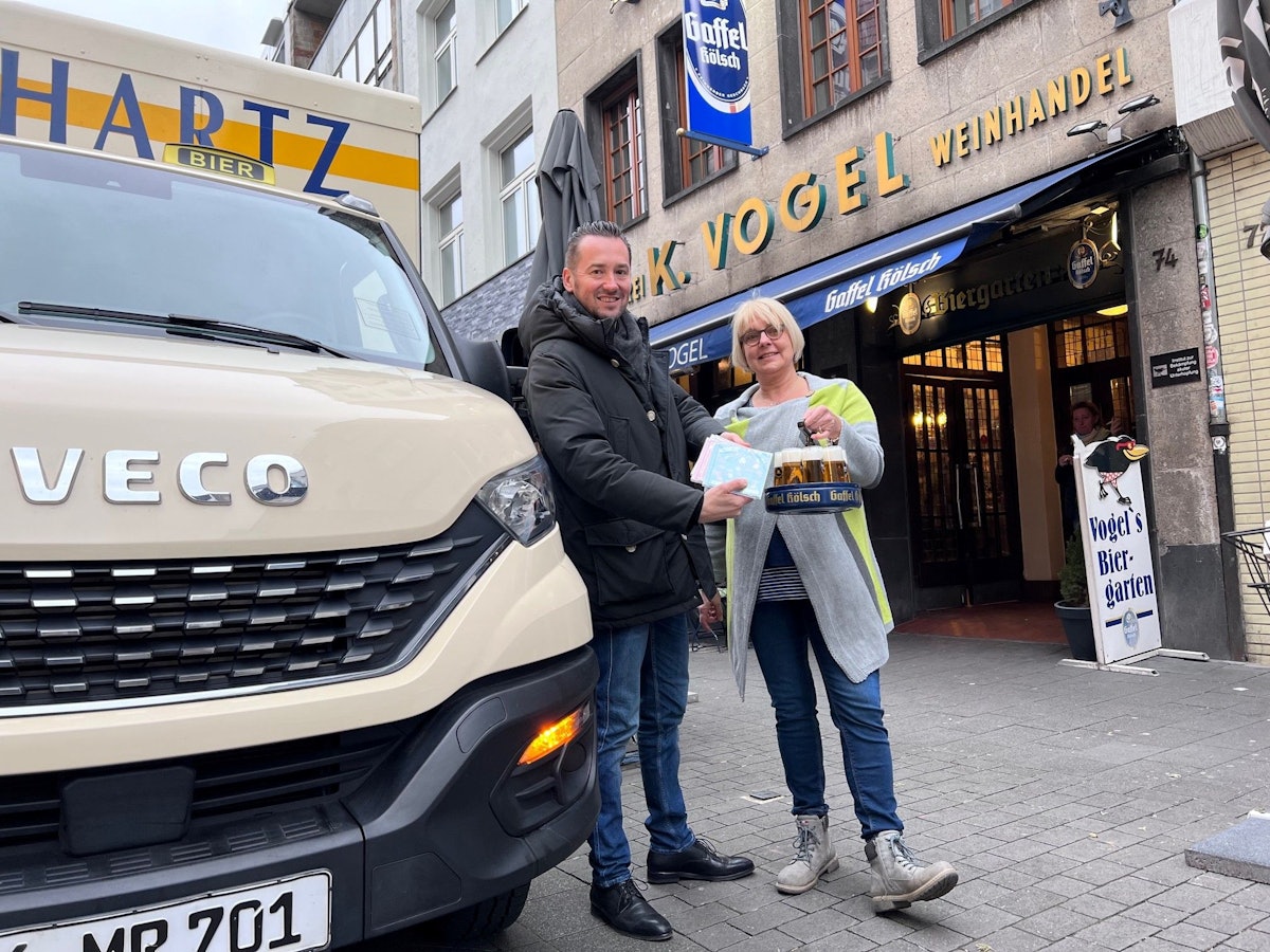 Bierlieferant Daniel Siebert (l.) übergibt am Eigelstein der Inhaberin des Weinhaus Vogel, Angelika, CDs.