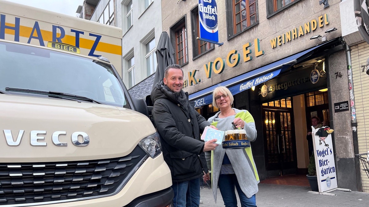 Bierlieferant Daniel Siebert (l.) übergibt am Eigelstein der Inhaberin des Weinhaus Vogel, Angelika, CDs.