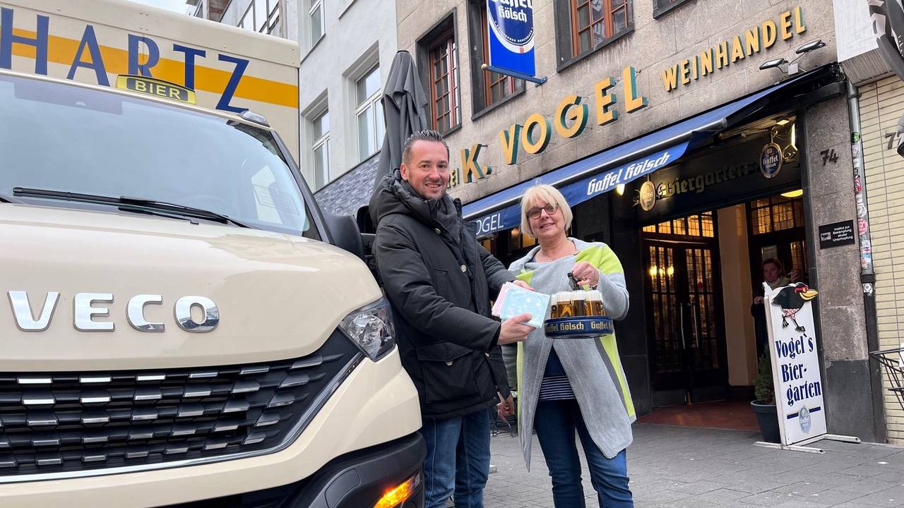 Bierlieferant Daniel Siebert (l.) übergibt am Eigelstein der Inhaberin des Weinhaus Vogel, Angelika, CDs.