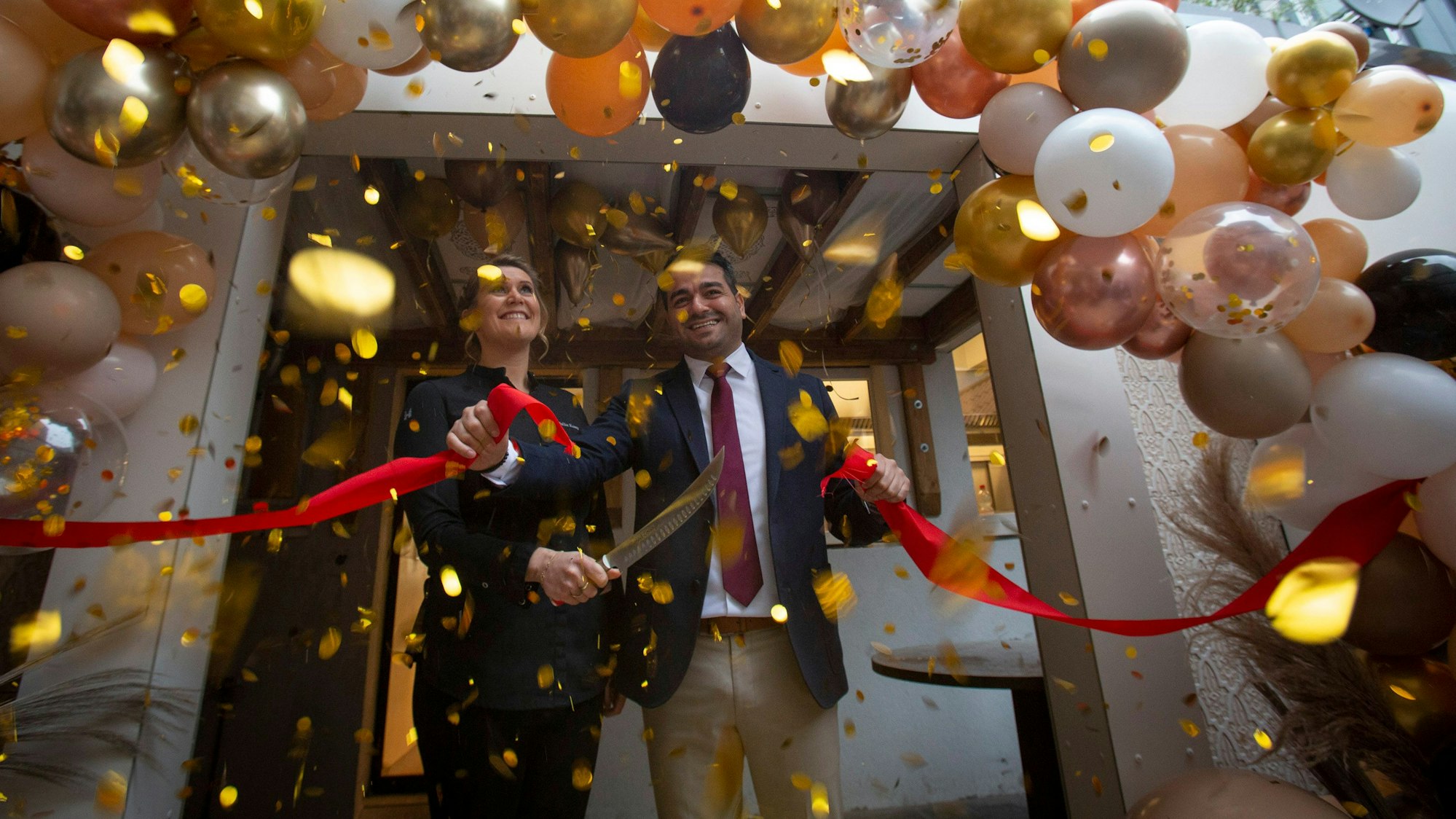Julia Komp und Yunus Özananar durchschneiden ein rotes Band, drumherum sind viele Luftballons
