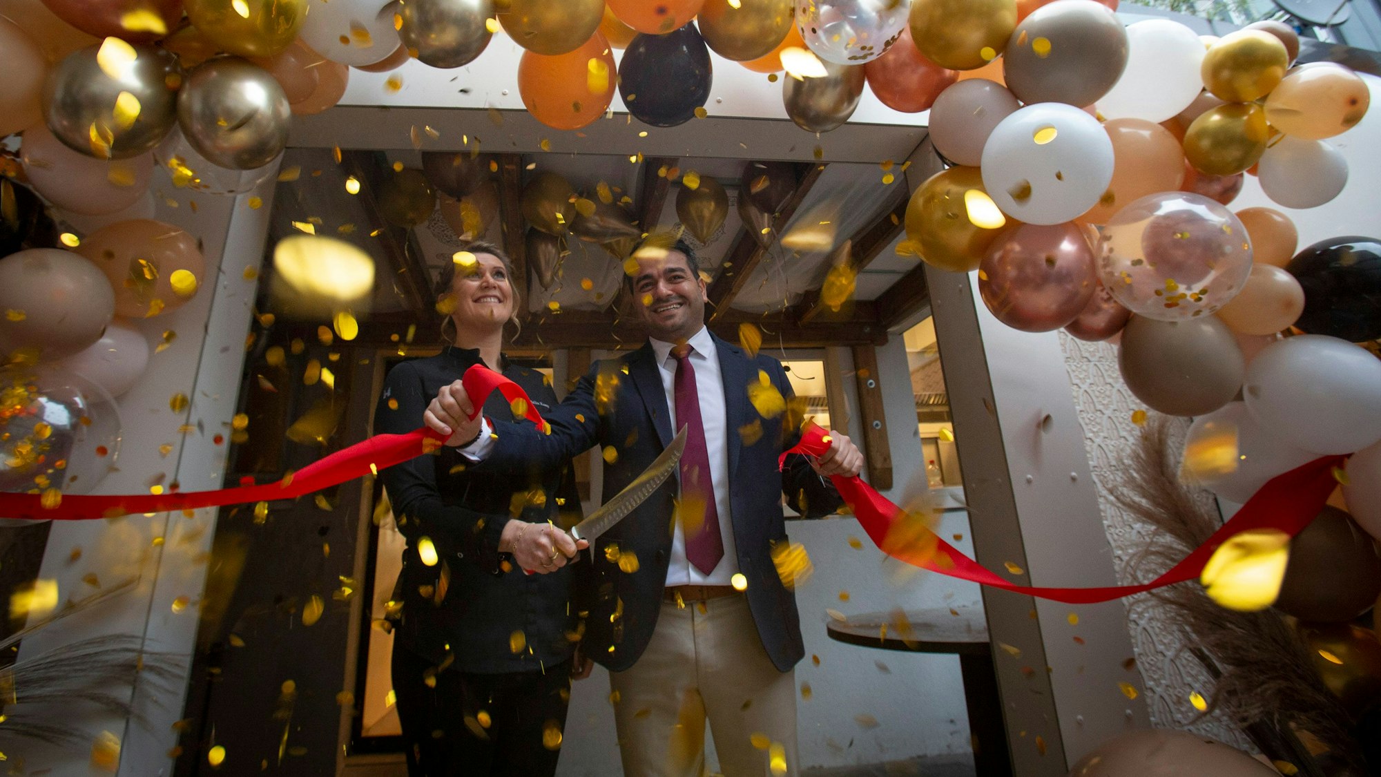Julia Komp und Yunus Özananar durchschneiden ein rotes Band, drumherum sind viele Luftballons